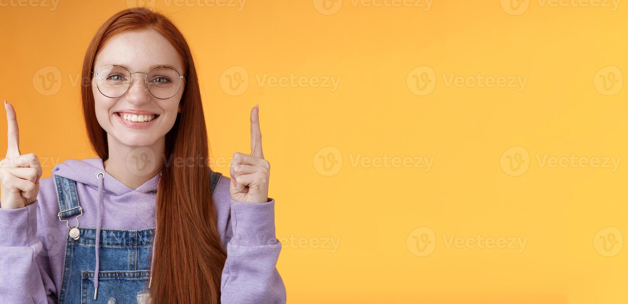 Lively charismatic pleasant redhead female student helpful pointing up index fingers showing awesome promo offer smiling delighted white teeth indicating advertisement recommend use product photo