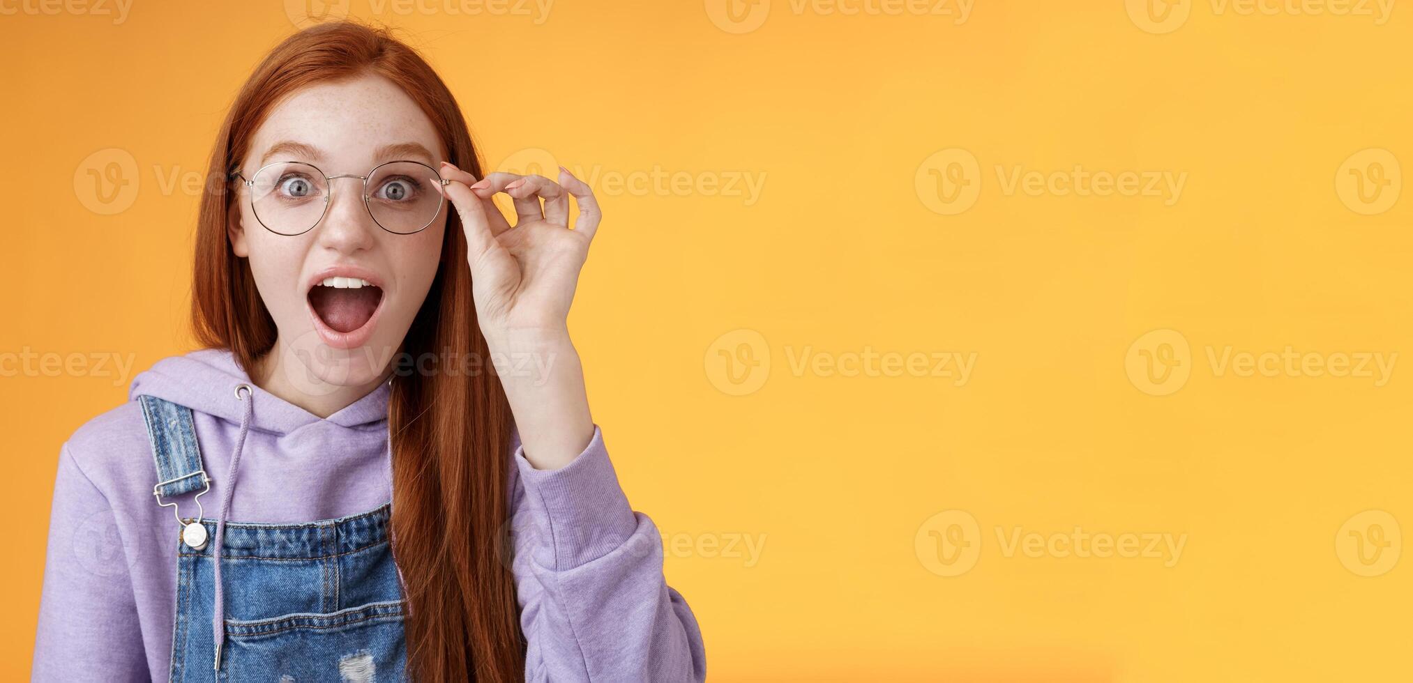 Dios mio entonces Frío. retrato asombrado Sin palabras emocionado pelirrojo niña soltar mandíbula divertido mirar fijamente cámara sorprendido encontrar fuera increíble producto red toque lentes leyendo impresionante correo, naranja antecedentes foto