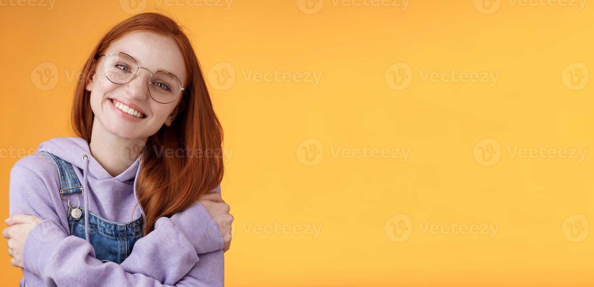 Tender romantic european redhead girlfriend tilting head cute lovely smile white teeth tilting head hugging herself wearing best friends hoodie adore new outfit grinning joyfully, orange background photo