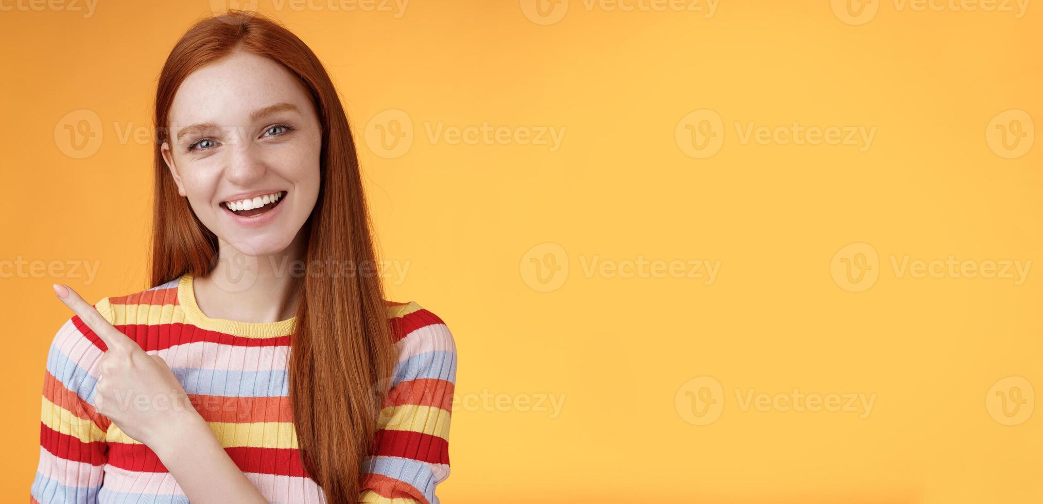 Friendly outgoing good-looking ginger girl university student discussing lecture classmate smiling laughing pointing upper left corner questioned curious know details standing orange background photo