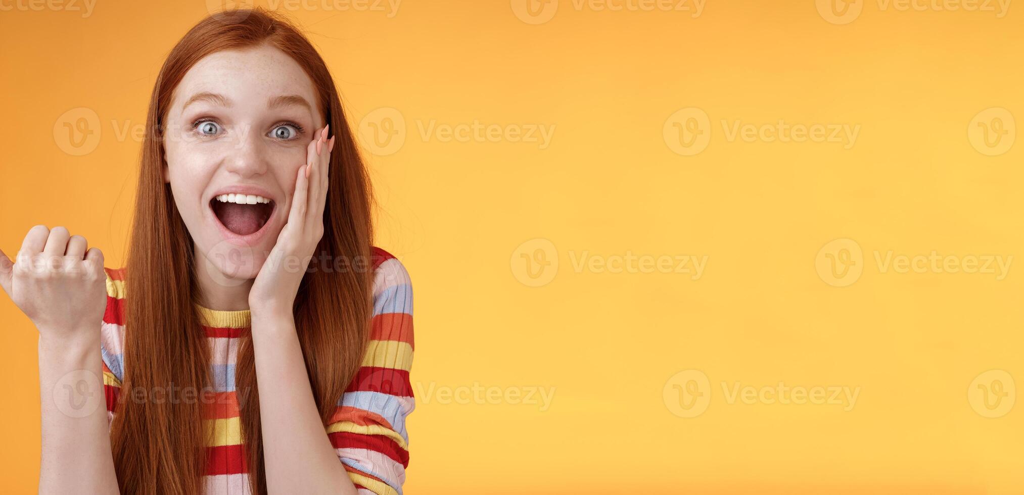 Cheerful excited impressed talkative girl pointing astonished thumb left drop jaw smiling broadly touch cheek thrilled, interesting event discuss awesome wonderful performance, orange background photo