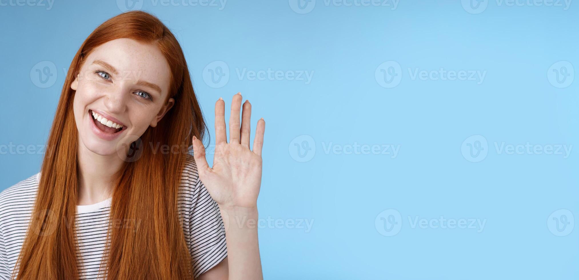 Attractive confident redhead sassy girl pure clean skin blue eyes tilting head cheerfully waving hand hello hi gesture greeting you look camera friendly welcoming friend, standing studio background photo