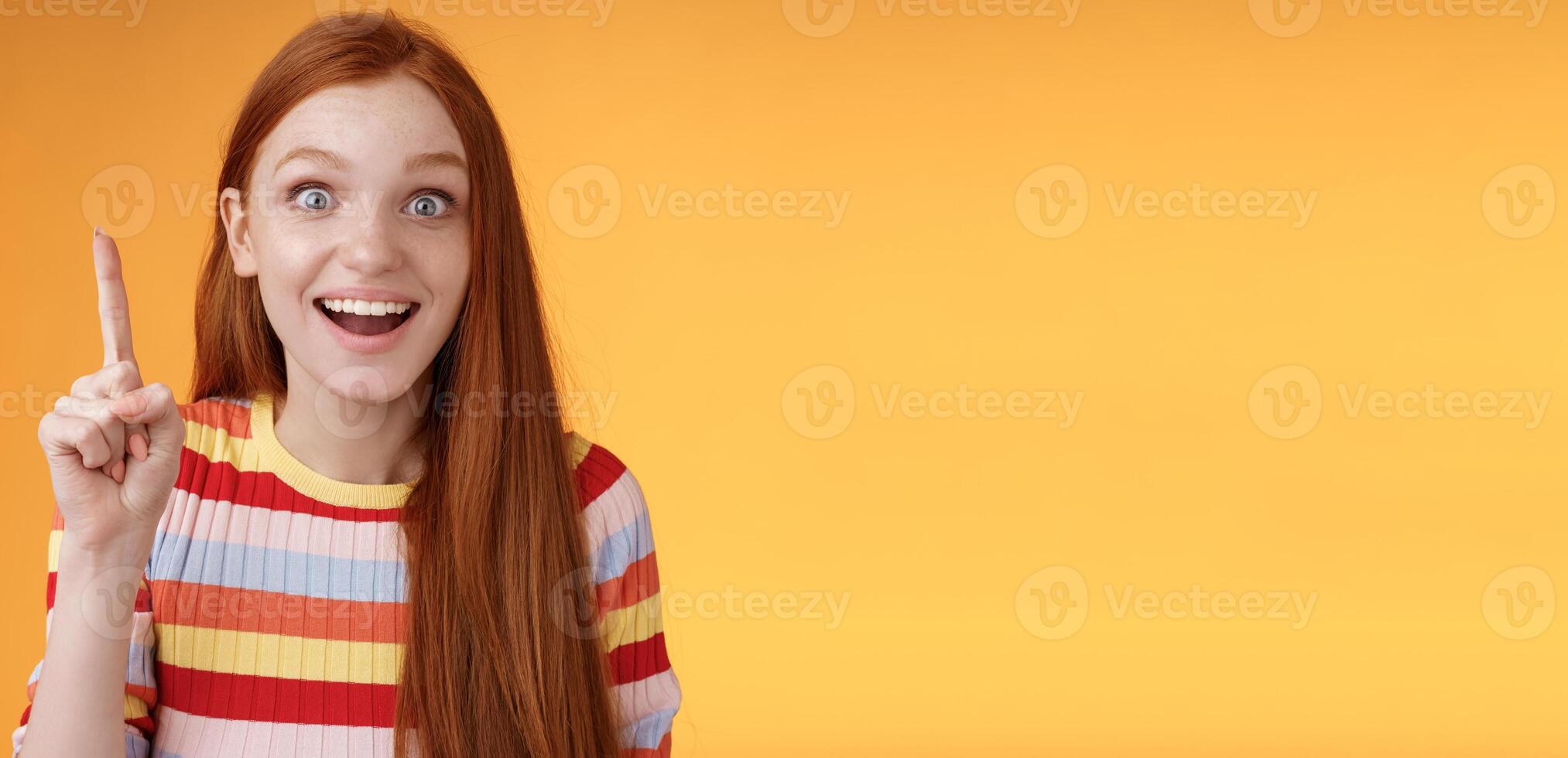 Excited happy cheerful young redhead female student got idea think answer raising index finger eureka gesture smiling thrilled wide eyes saying plan have excellent suggestion, orange background photo