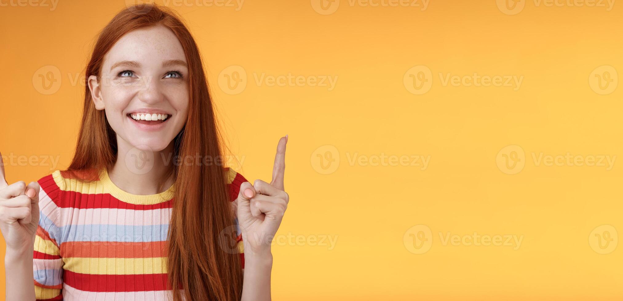 Happy cheerful redhead girl having fun amusement park laughing joyfully pointing look up index fingers upwards enjoy entertainment standing orange background amused grinning joyfully photo