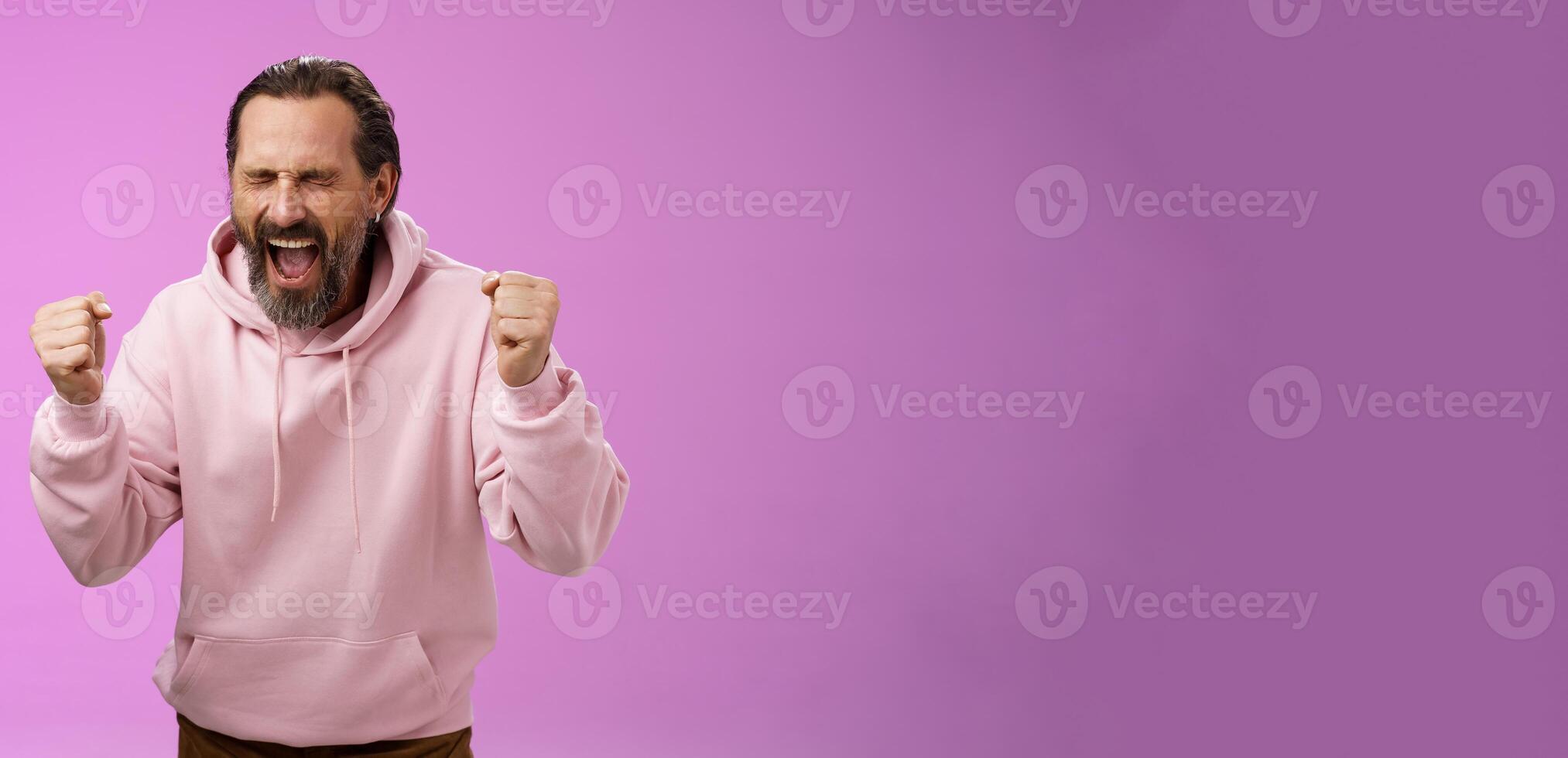 Accomplished happy joyful triumphing mature 40s bearded man grey hair yelling yes thrilled joyfully clench fists celebrating success win lottery become millionaire, standing purple background photo