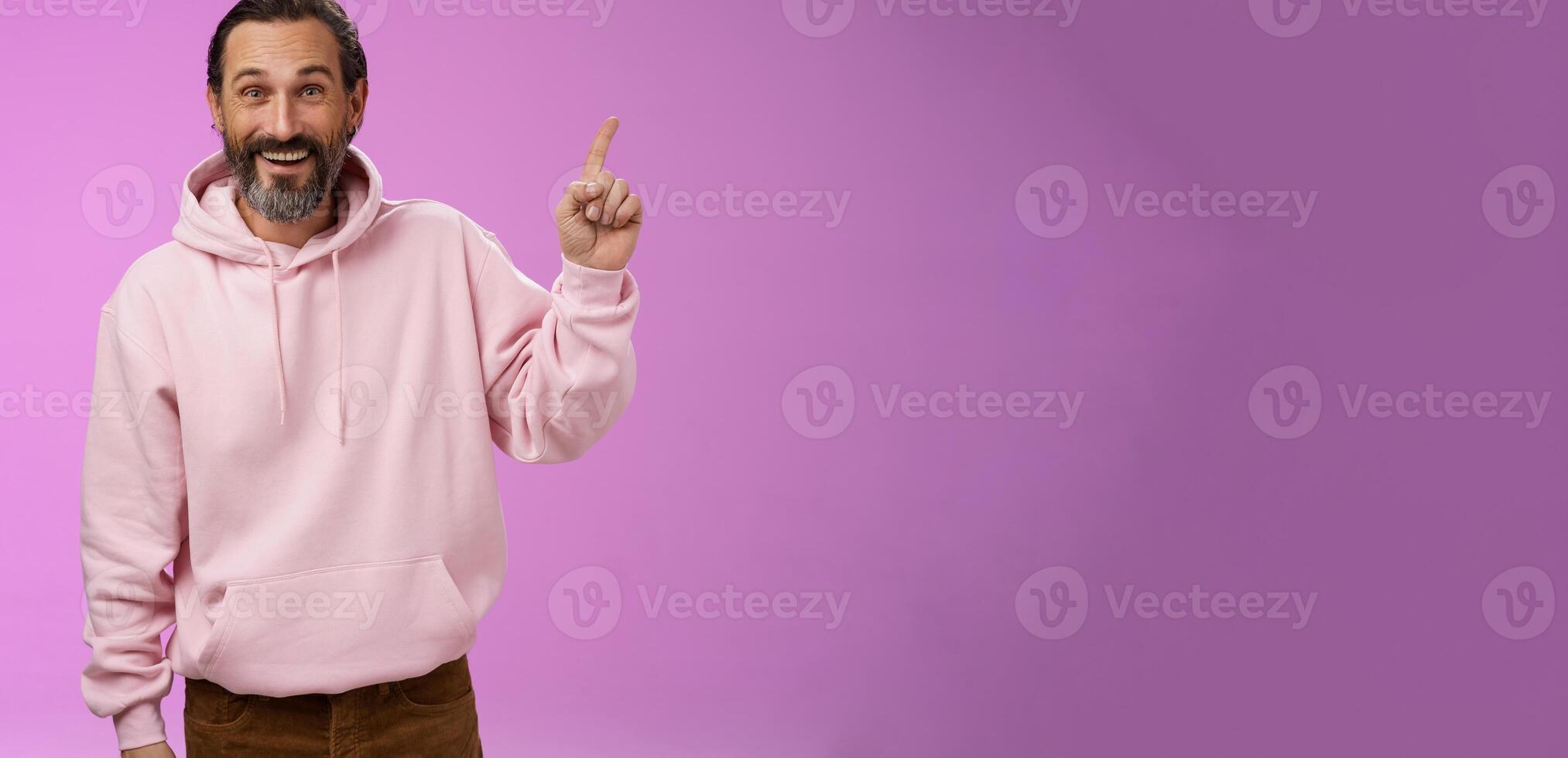 Handsome excited mature 40s bearded man wrinkles grey hair laughing happily acting immature having fun amusing vacation trip pointing up astonished smiling impressed surprised, purple background photo