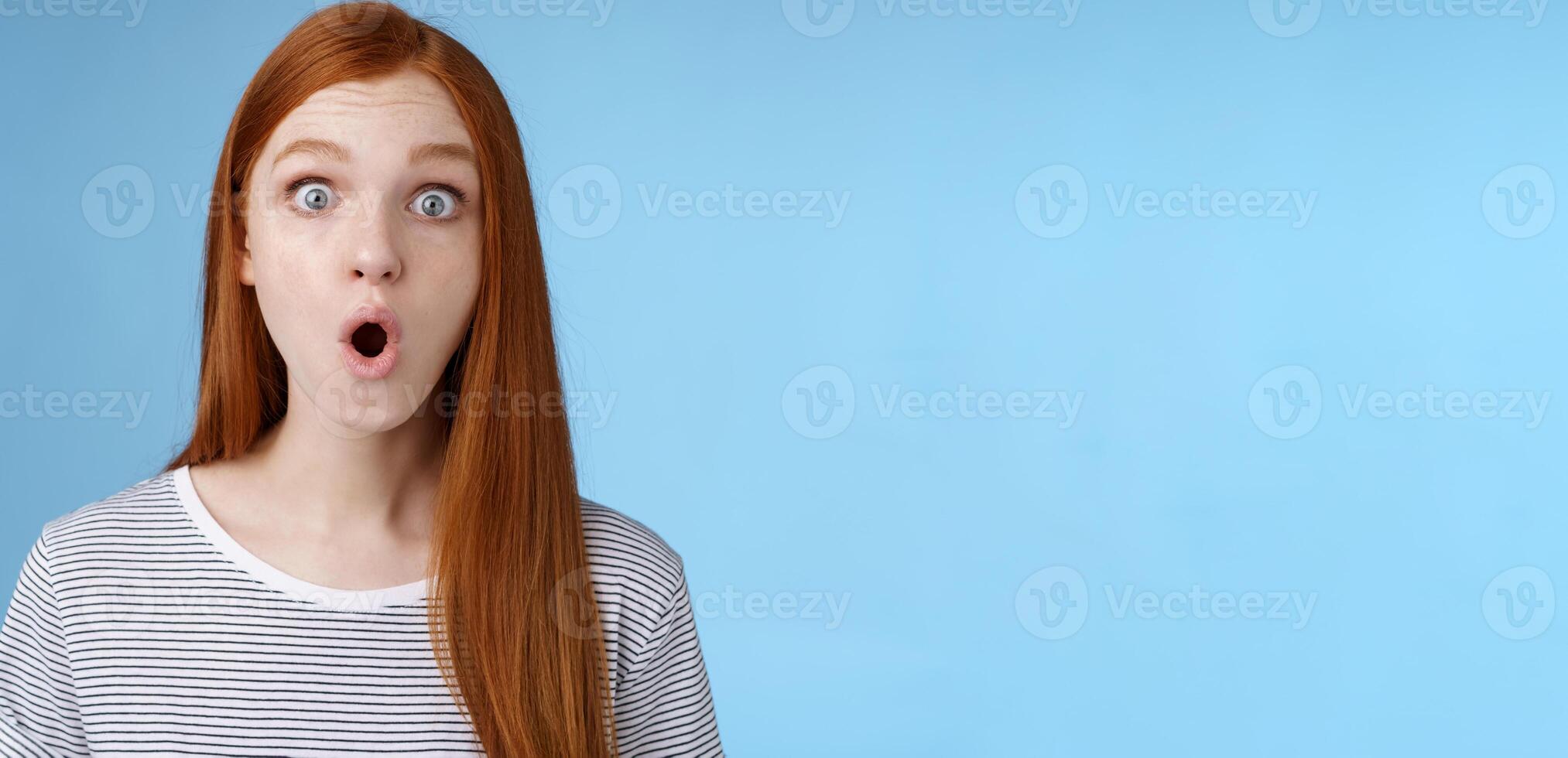 Wow omg fascinating. Impressed surprised amused good-looking redhead girl folding lips astonished wide eyes stunned reacting incredible cool promo standing blue background speechless photo