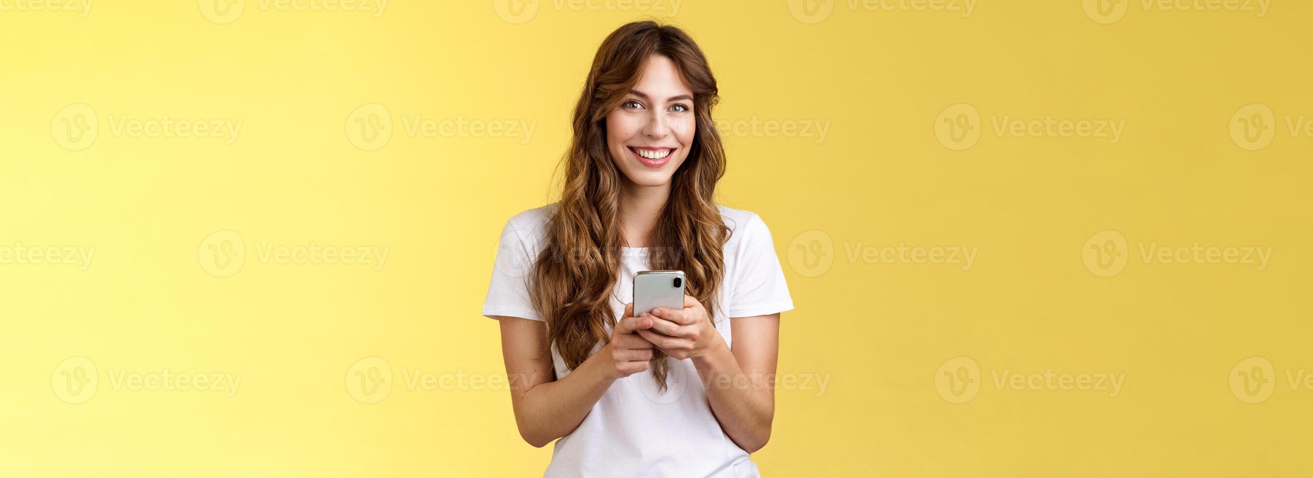 entusiasta encantador sociable joven niña mensajería amigo enviando fotos social medios de comunicación sostener teléfono inteligente Mira cámara felizmente simpático sonriente estar amarillo antecedentes casual atuendo