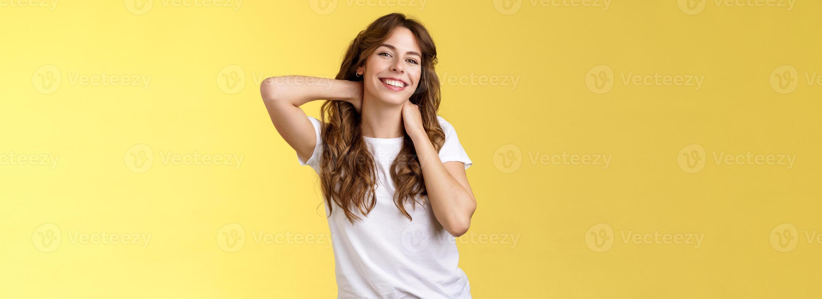 Cheerful charismatic good-looking curly-haired woman stretching posing yellow background touch neck flirty smiling relaxing perfect summer vacation booking weekend trip finally rest under sun photo