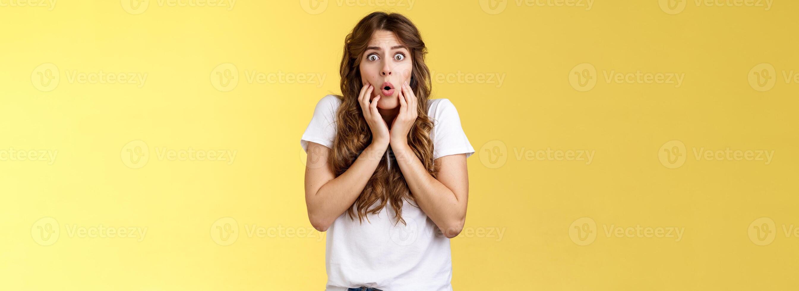 Pity upset worried cute curly-haired girl frowning feel sorry for friend pulling sorrow face touch cheeks gasping distressed express empathy shook stand yellow background anxious terrified photo