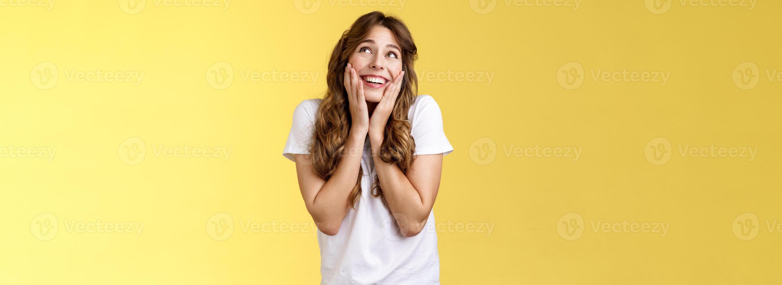 Dreamy flirty feminine cute female curly hairstyle sighing lovely admiration look up smiling broadly touch cheeks blushing recall heartwarming romantic date express tempation joy yellow background photo