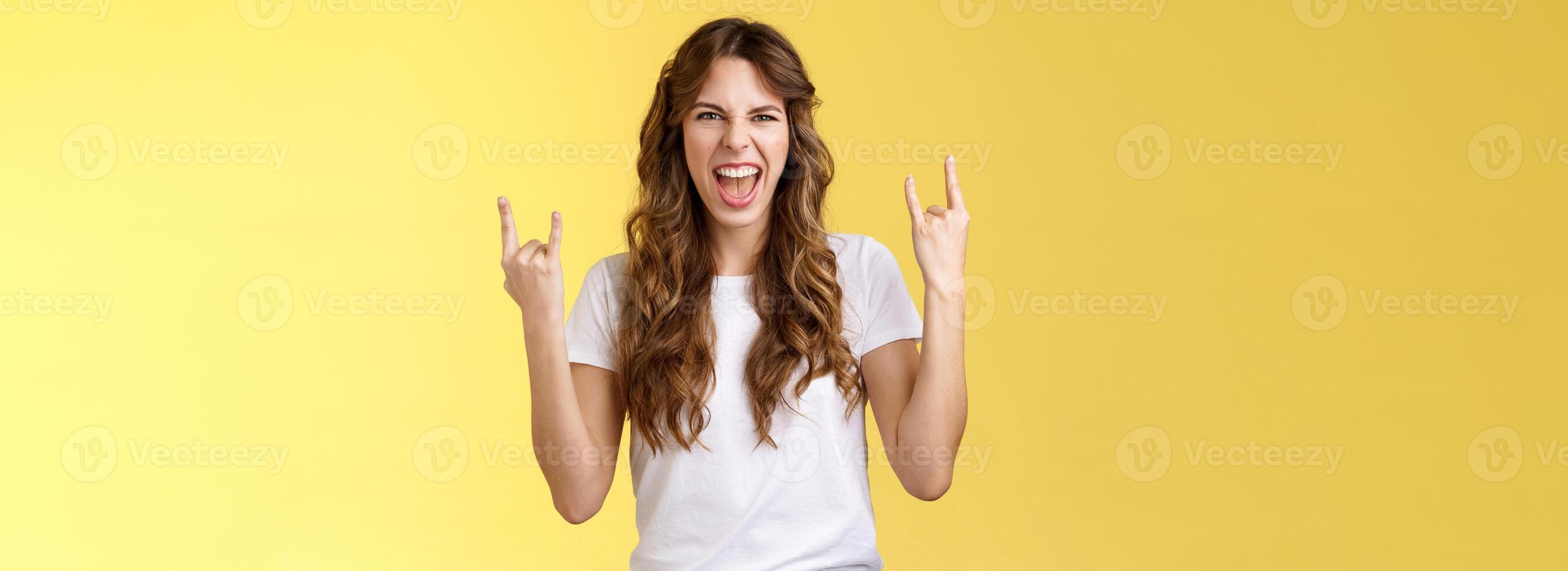 Going wild. Daring amused good-looking european curly-haired girl acting thrilled excited having fun enjoy awesome concert show yeah rock-n-roll heavy metal gesture grimacing satisfied photo