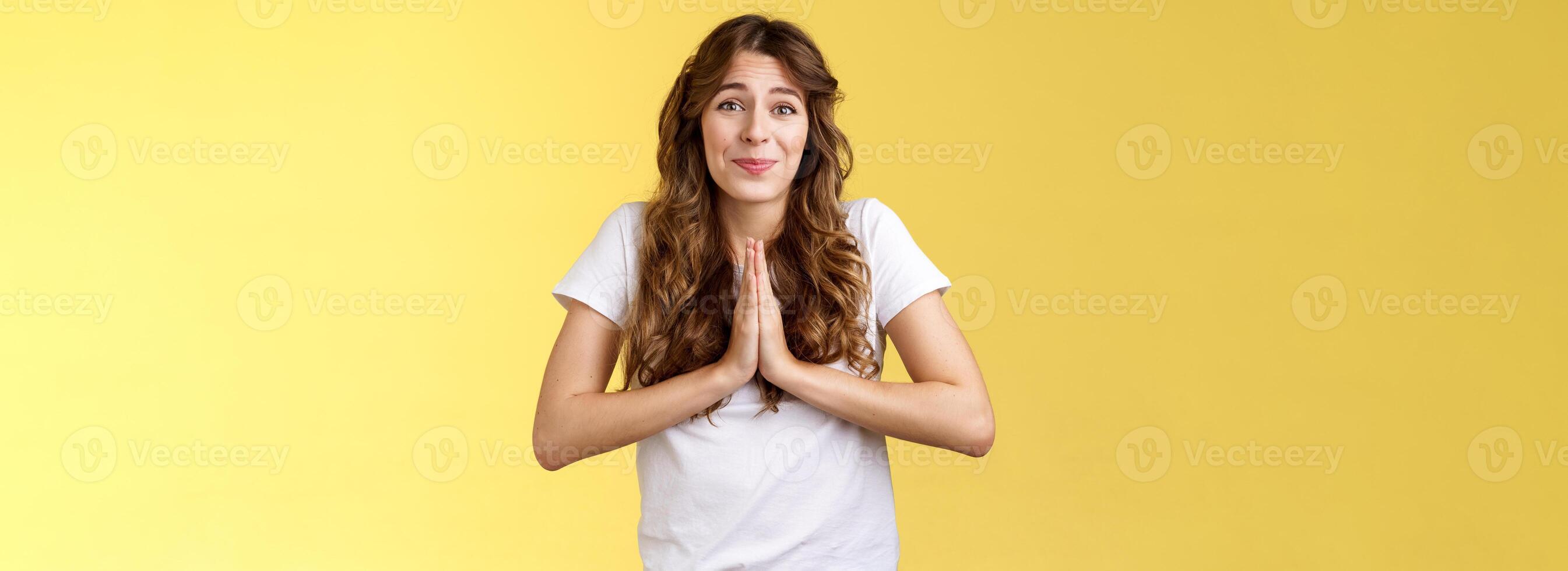 Cute hopeful young caucasian girl stooping hold hands pray smiling hope for pity begging favour plead asking advice say sorry grinning lovely making faithful glances you lend hand yellow background photo