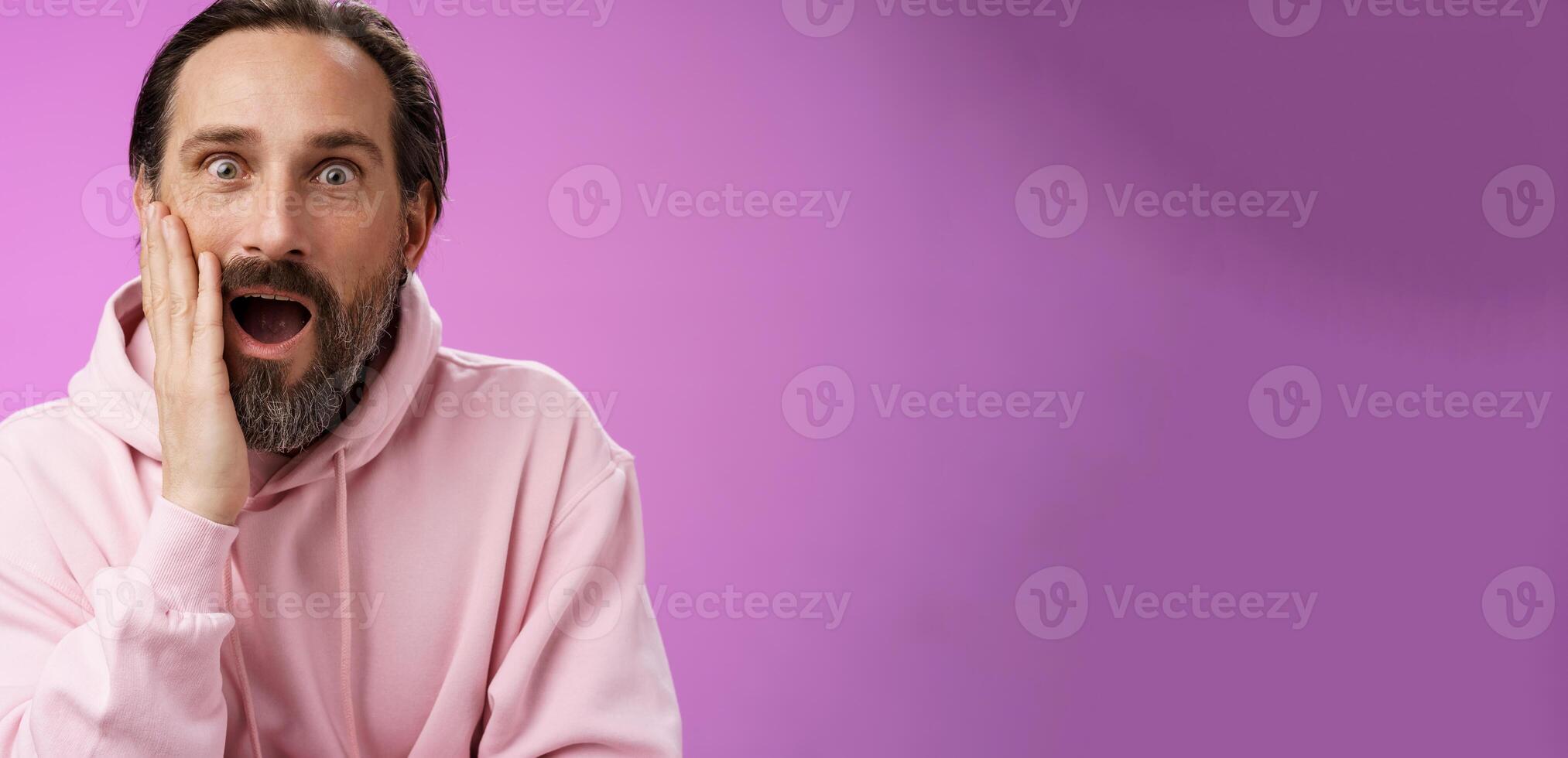 Impressed fascinated speechless mature male attend interesting lecture drop jaw thrilled touch cheek palm widen eyes surpised astonished, standing purple background amzed and amused photo