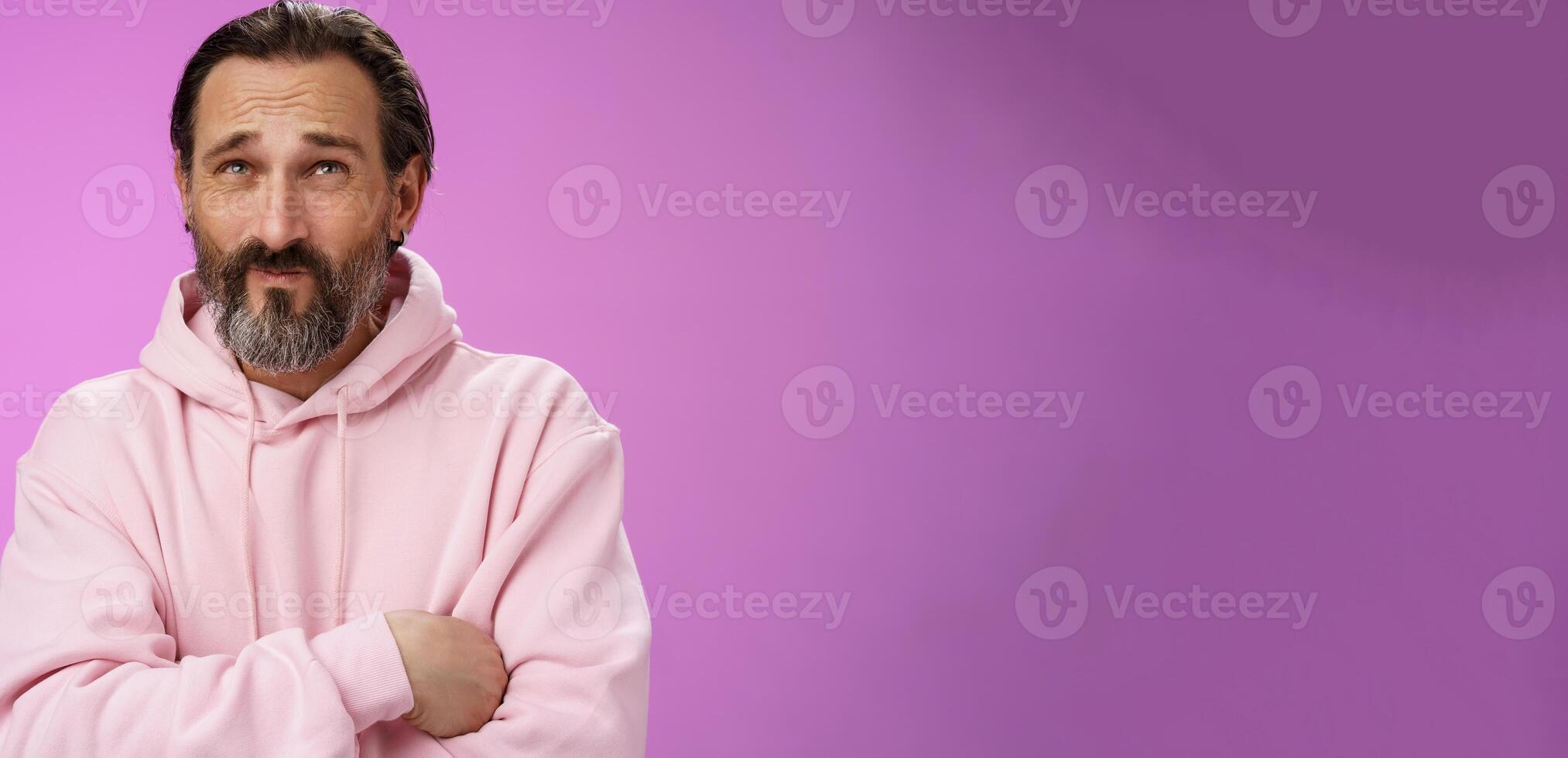 Unsure troubled caucasian bearded adult guy with earring pink hoodie press lips frowning counting mind standing hesitant doubtful thinking look up uncertain taking important decision photo