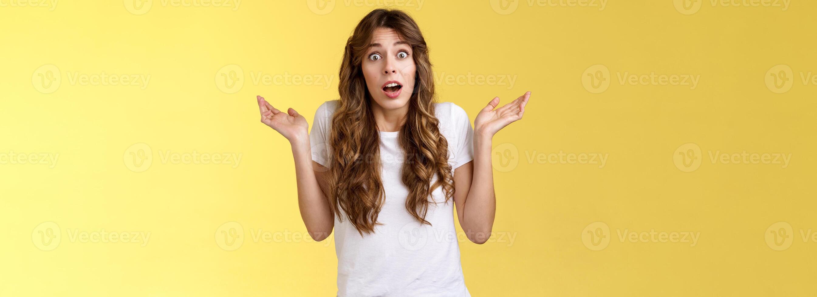 I not know. Clueless confused cute nervous young woman shrugging hands raised sideways full disbelief questioned expression lift eyebrows puzzled unable answer question stand yellow background photo