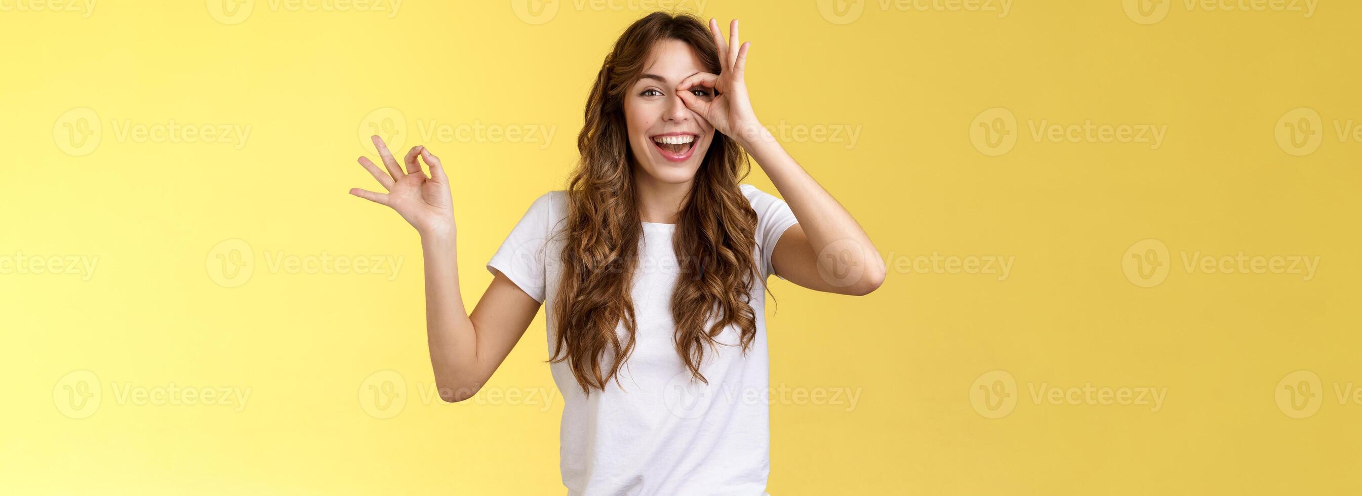 Friendly charismatic enthusiastic happy woman having perfect day show okay ok circle gesture look through ring amused wondered smiling broadly delighted express joy admiration yellow background photo