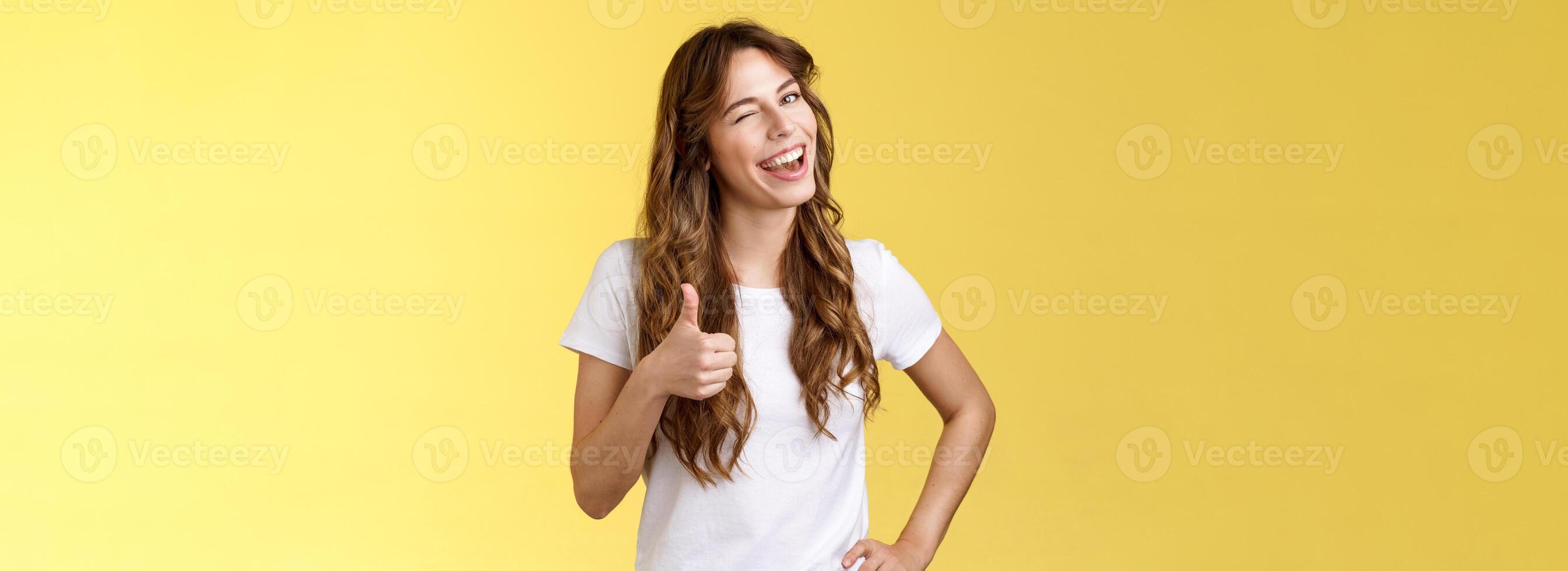 I support you guys good luck. Happy cheerful cheeky attractive girl wink approval like show thumb up smiling broadly satisfied awesome party congratulating friend well done yellow background photo