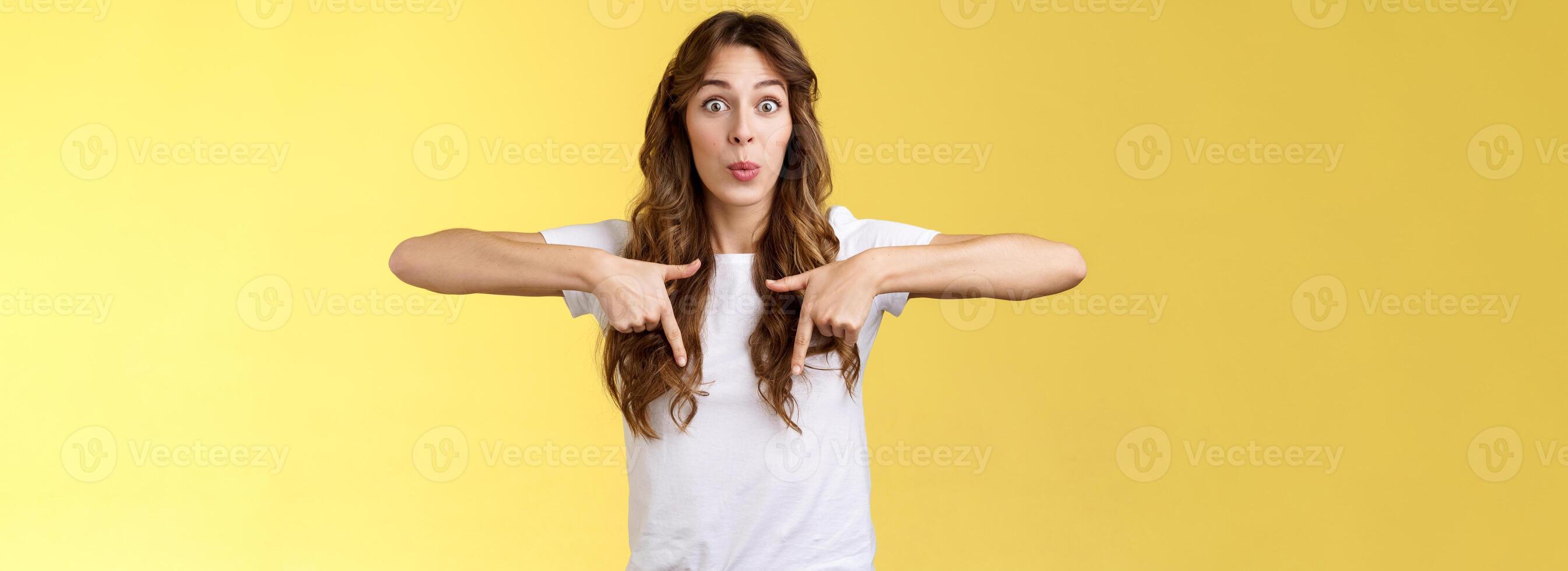 Fascinated impressed charismatic brunette female curly long haircut folding lips whistle astonished react excited thrilled telling you incredible promotion pointing down bottom yellow background photo