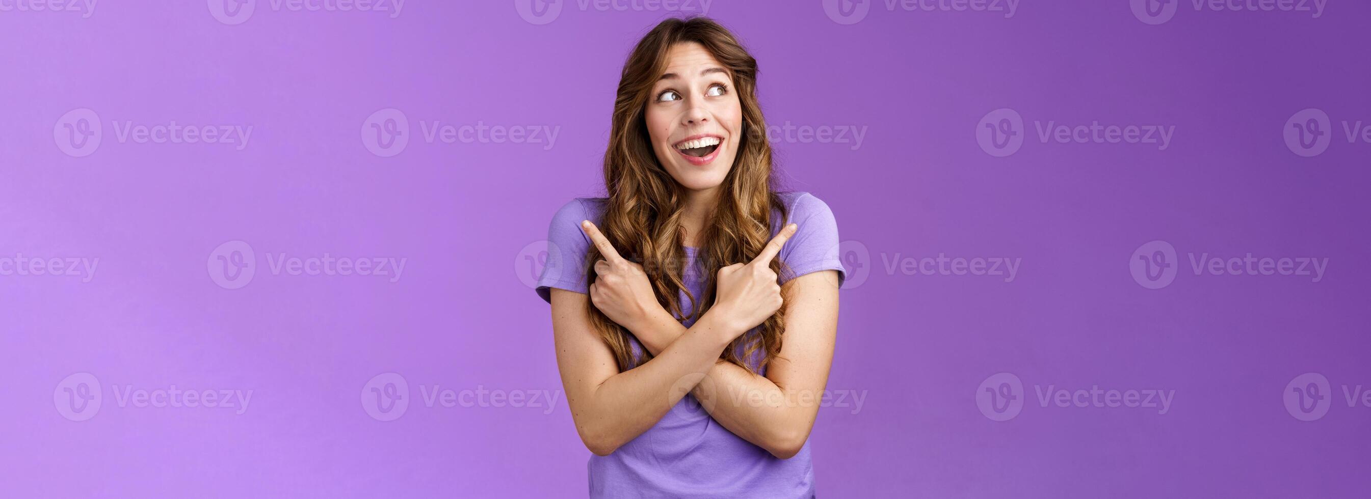 Happy cheerful lively curly girl smiling broadly receive awesome opportunity study abroad choosing universities cross hands sideways pointing left right grinning amused entertained purple wall photo