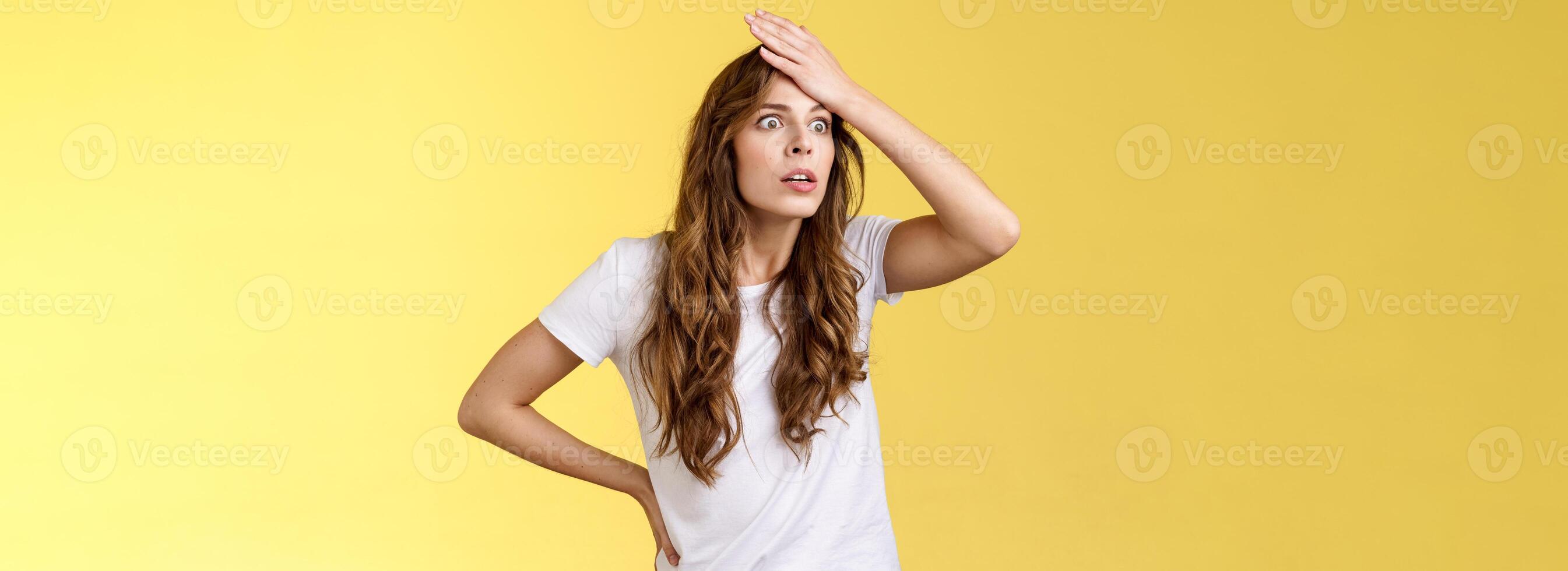 Oh gosh how stupid. Shocked embarrassed ambushed curly-haired girl popping eyes punch forehead make facepalm gasping stare aside bothered forgot cancel appointment stand yellow background photo