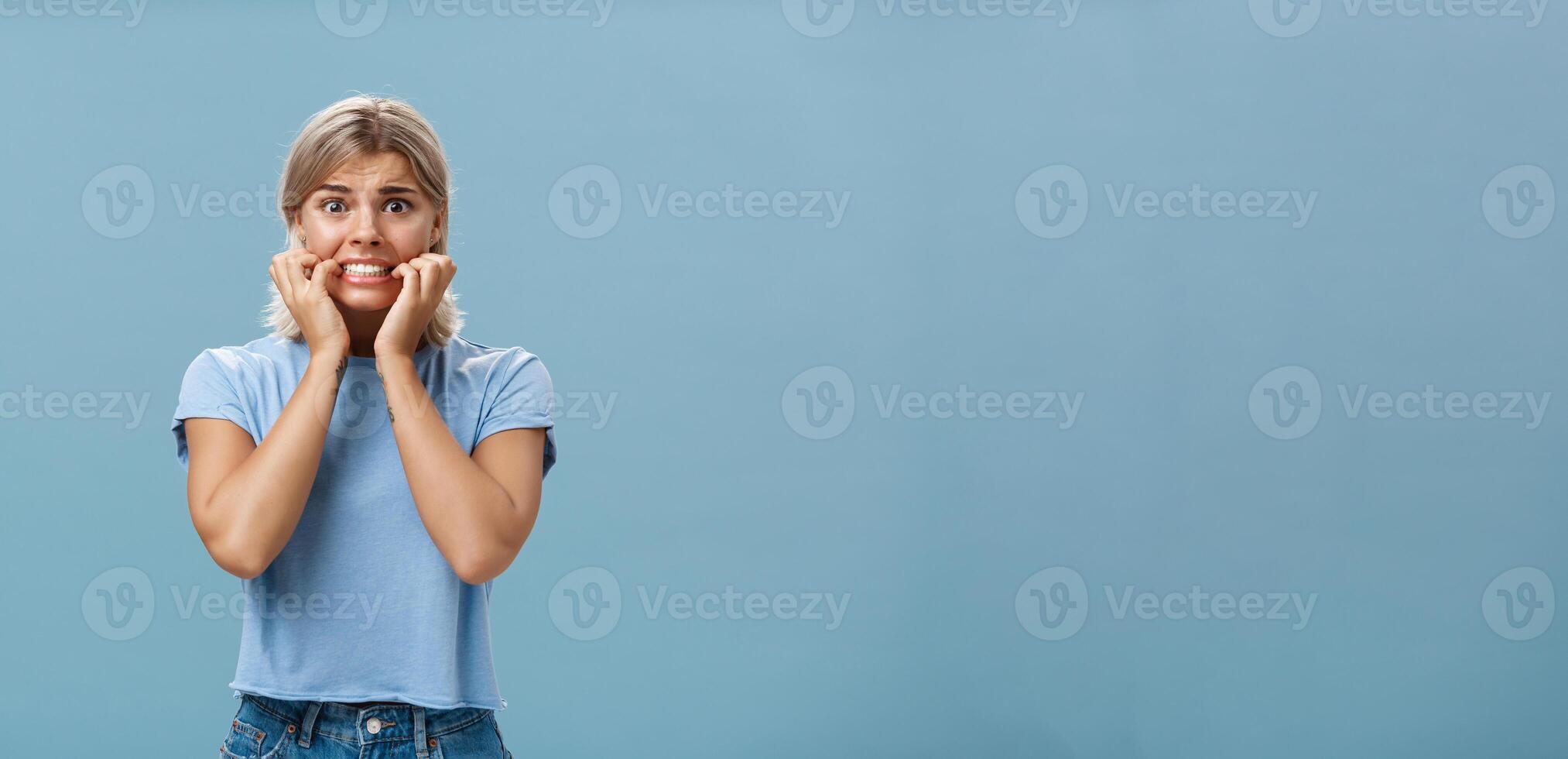 Gosh scary movies makes me tremble. Portrait of worried young attractive and stylish woman starting panic and nervous clenching teeth holding hands near mouth and frowning looking concerned and scared photo