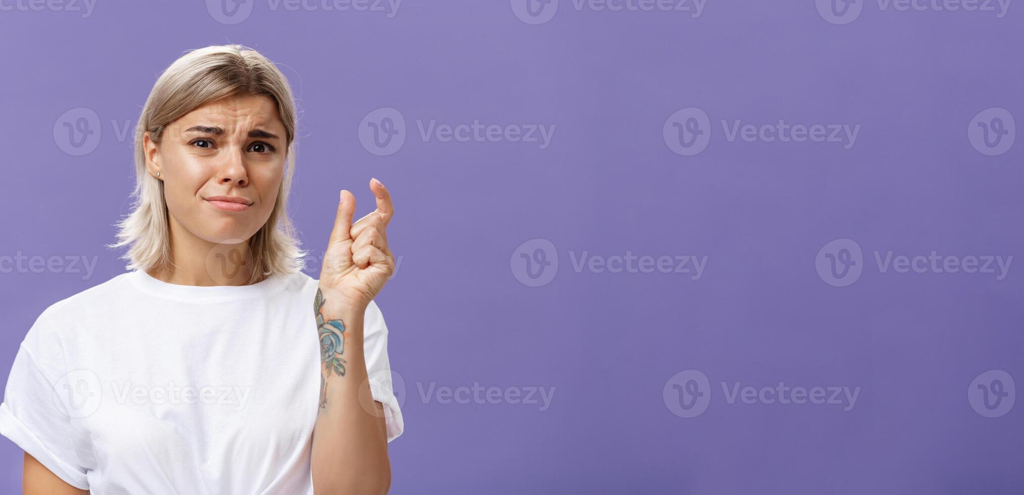 Woman feeling regret lacking small amount of money to afford car. Unhappy displeased good-looking stylish female with tattoos on hands frowning and pursing lips shaping tiny or little object photo