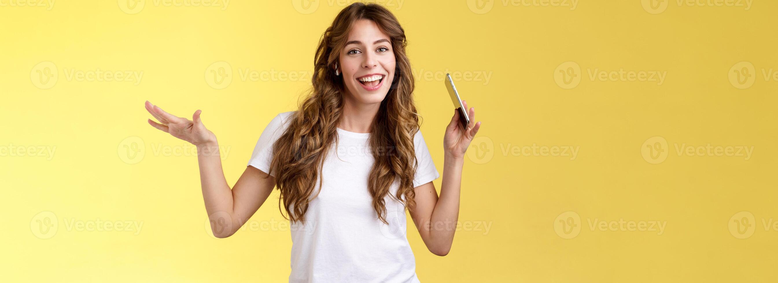 Sassy cheerful carefree attractive modern girl curly hairstyle having fun lively upbeat mood moving body rhythm shake hands hold smartphone lip sync wear wireless earbuds listen music dancing photo