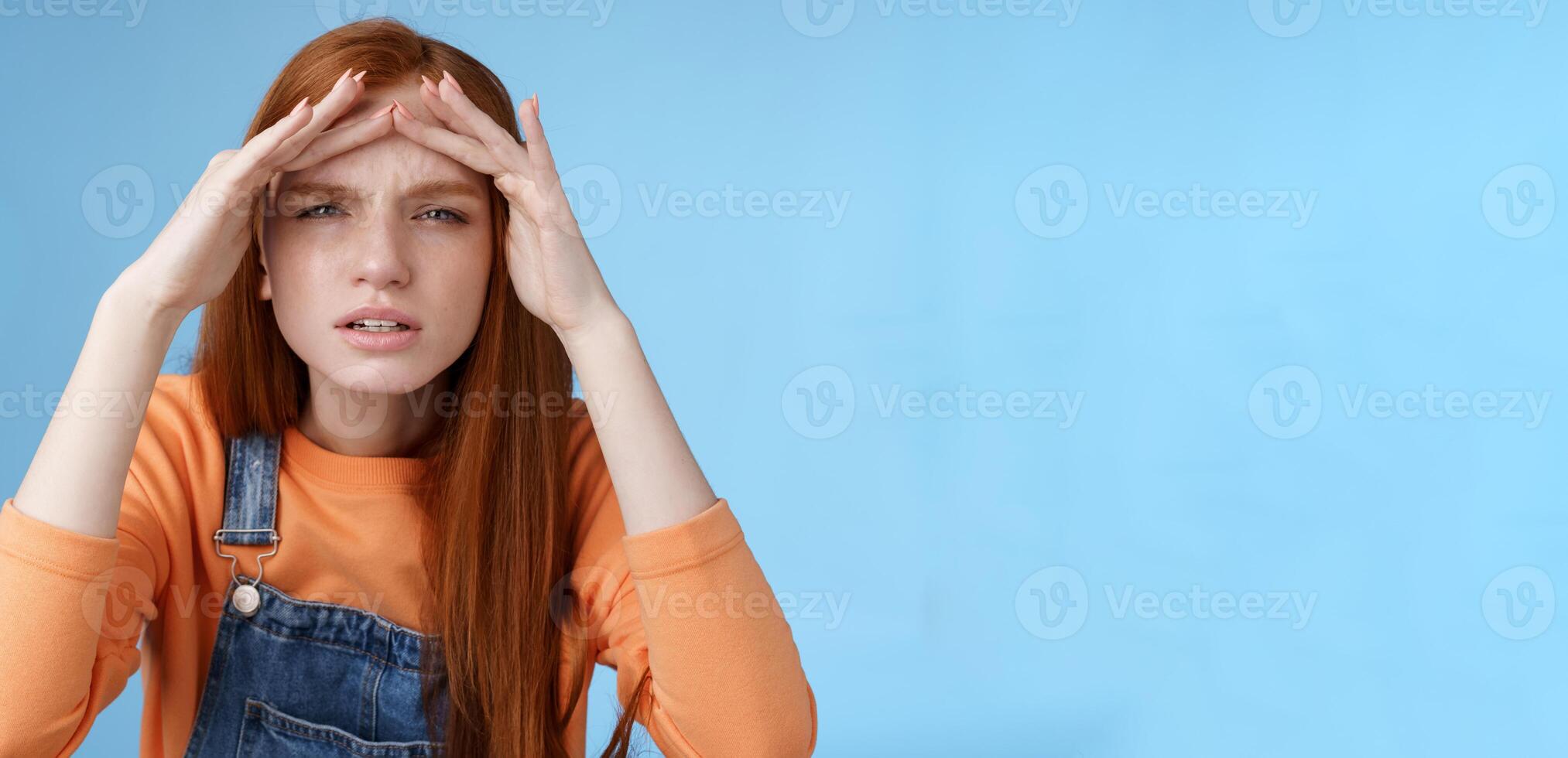 Puzzled unsure cute funny redhead european woman searching someone squinting cannot see without glasses peer into distance hold hands forehead cover sight sunlight, standing blue background photo