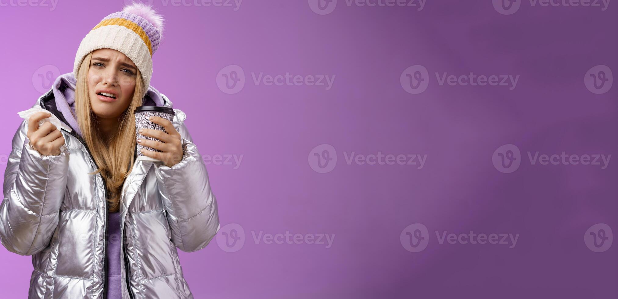 Upset dizzy cute blond girl got sick feel unwell grimacing hold hot tea take-away cup tissue sneezing suffering high temperature runny nose headache standing uncomfortable bad purple background photo