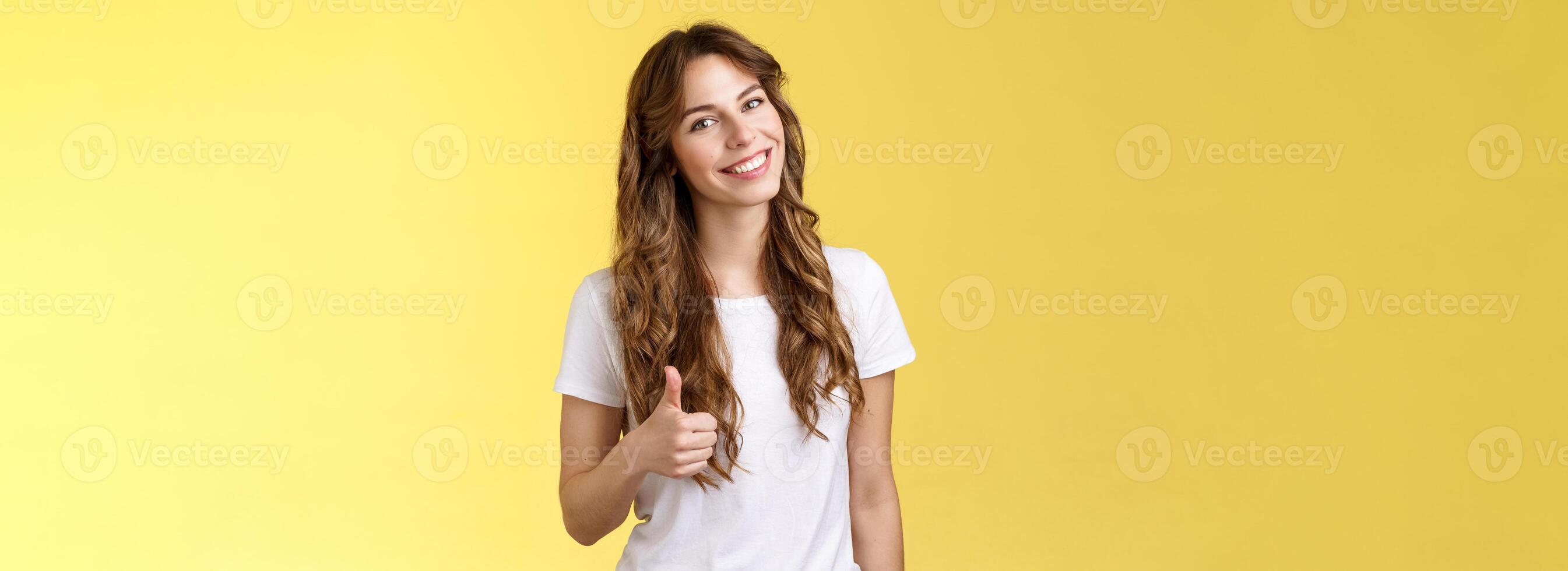 Well done congratulations. Happy charismatic pretty european female tilt head smiling broadly accept agree your idea like satisfied good result show thumb up approval gesture yellow background photo