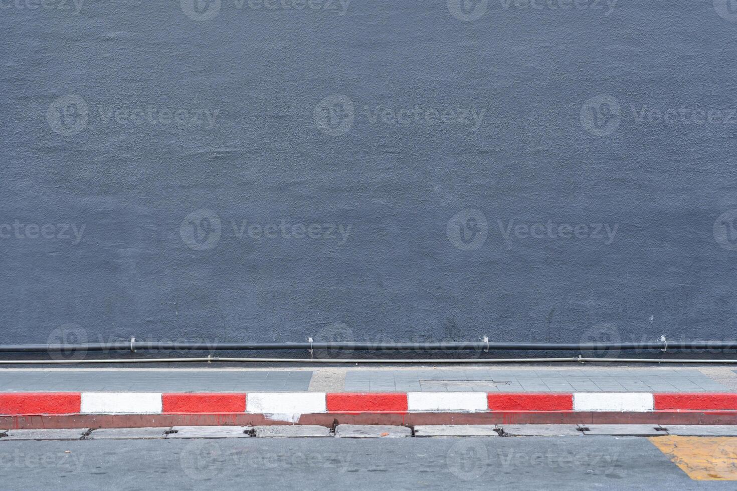 Gray Cement wall is with copy space. Plastered concrete wall background. Red and white stripes on footpath. Roadside street view background. photo