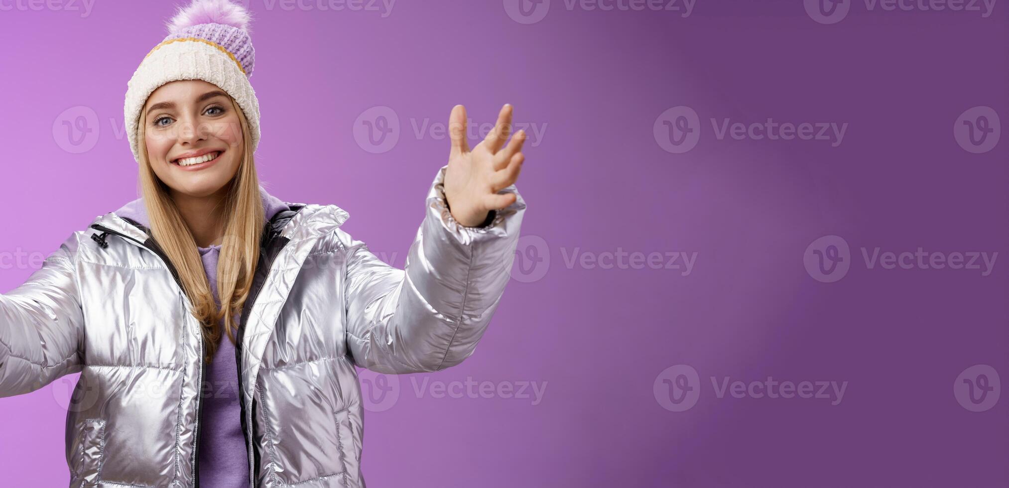 Friendly charming smiling european girl vacation wearing silver warm glittering jacket hat extend arms waiting girlfriend fall arms embrace loving person standing happily purple background photo