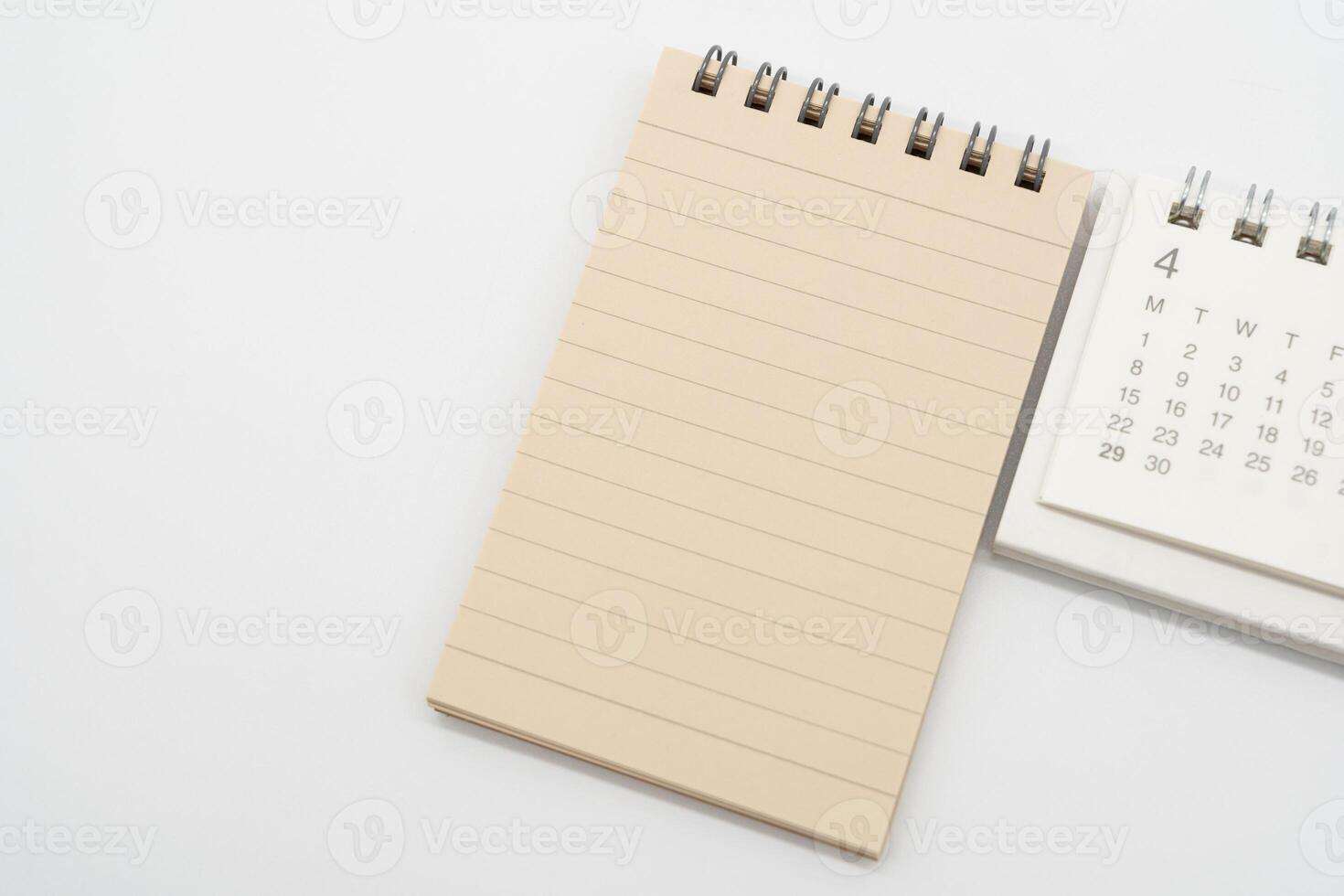 Empty Spiral notepad with brown lined papers and Simple desk calendar for APRIL in isolated background. Memo concept with copy space. photo