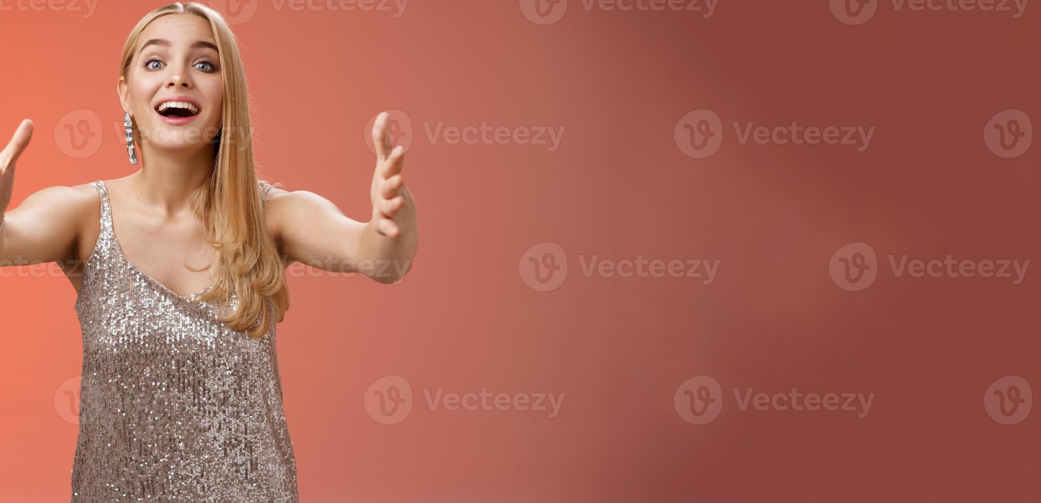 Excited charmign touched hearwarming young blond woman in silver party glamour dress stretch hands towards camera amused wanna hug cuddle hold cute puppy arms, standing red background photo