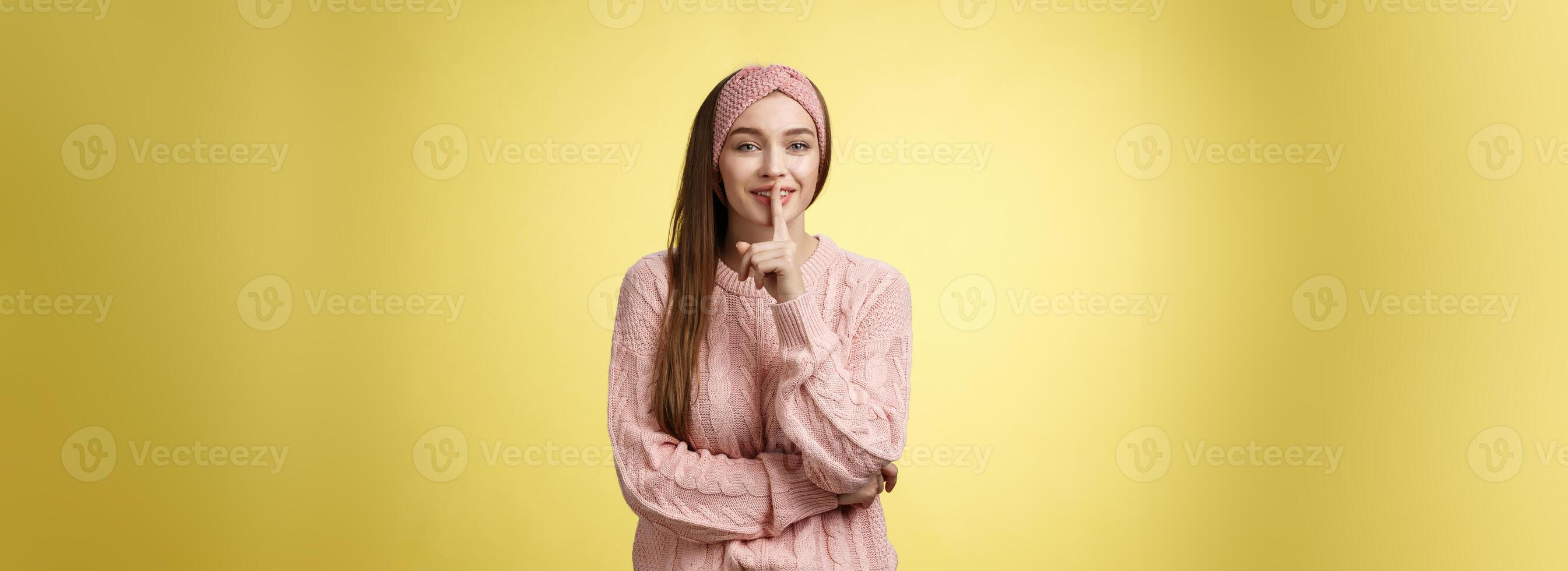 Shh keep voice down. Attractive glamour young stylish schoolgirl having secrets showing shush gesture, holding index finger on mouth smiling, hiding surprise asking not tell anyone over yellow wall photo