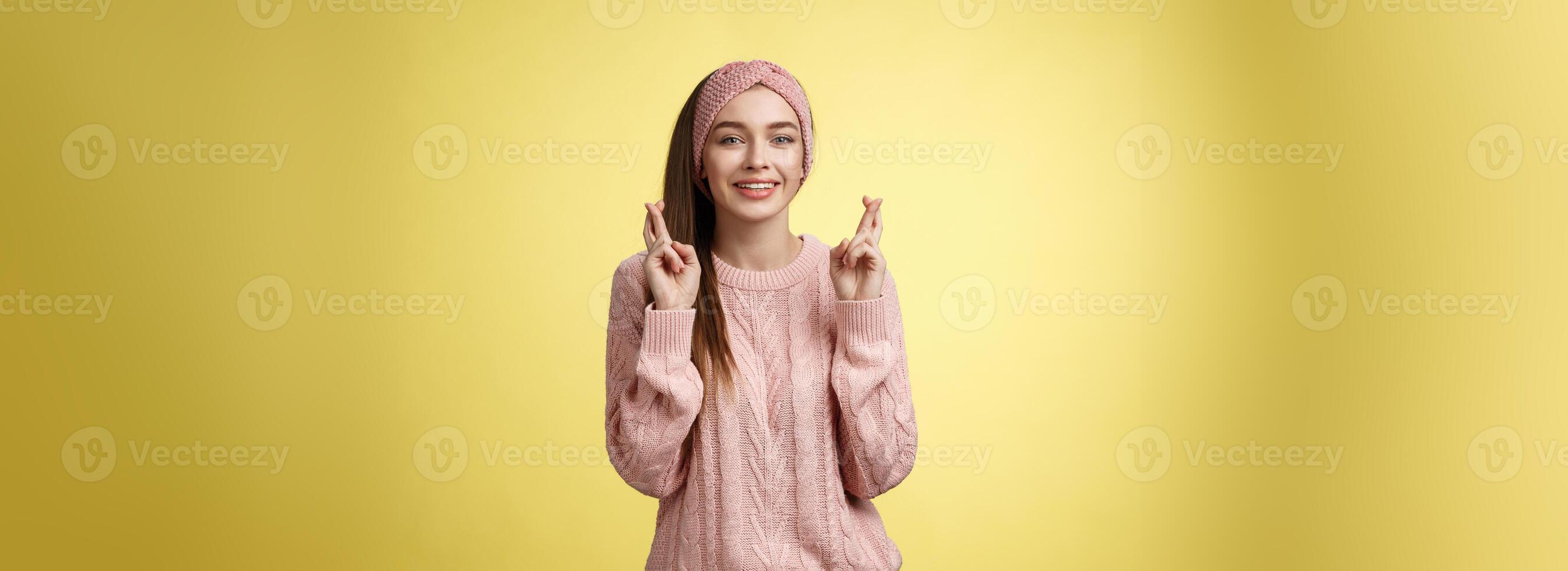 cruzar mi dedos para tú. apoyo linda joven europeo Novia vistiendo suéter, glamour venda haciendo suerte, deseo gesto sonriente esperanzado teniendo fe sueño ven cierto terminado amarillo antecedentes foto