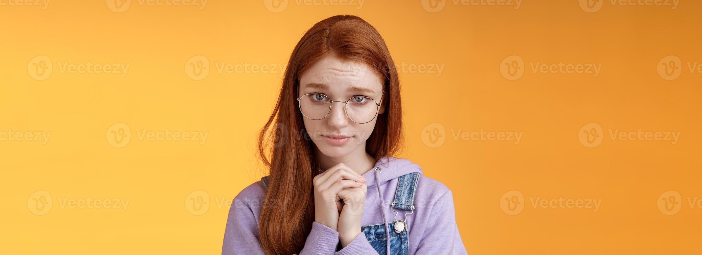 Silly guilty young shy redhead girlfriend asking forgiveness supplicating lower head look from under forehead frowning begging apology favour standing insecure sad pleading help, orange background photo