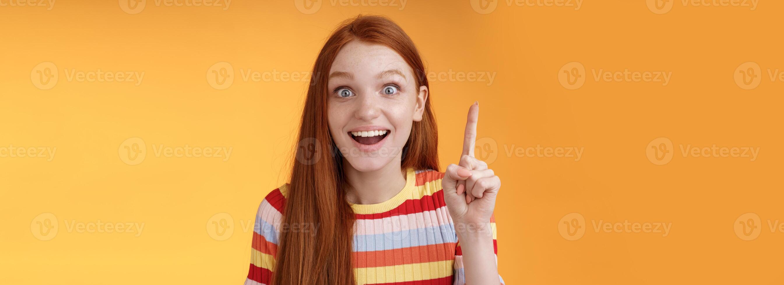 Excited happy cheerful young redhead female student got idea think answer raising index finger eureka gesture smiling thrilled wide eyes saying plan have excellent suggestion, orange background photo
