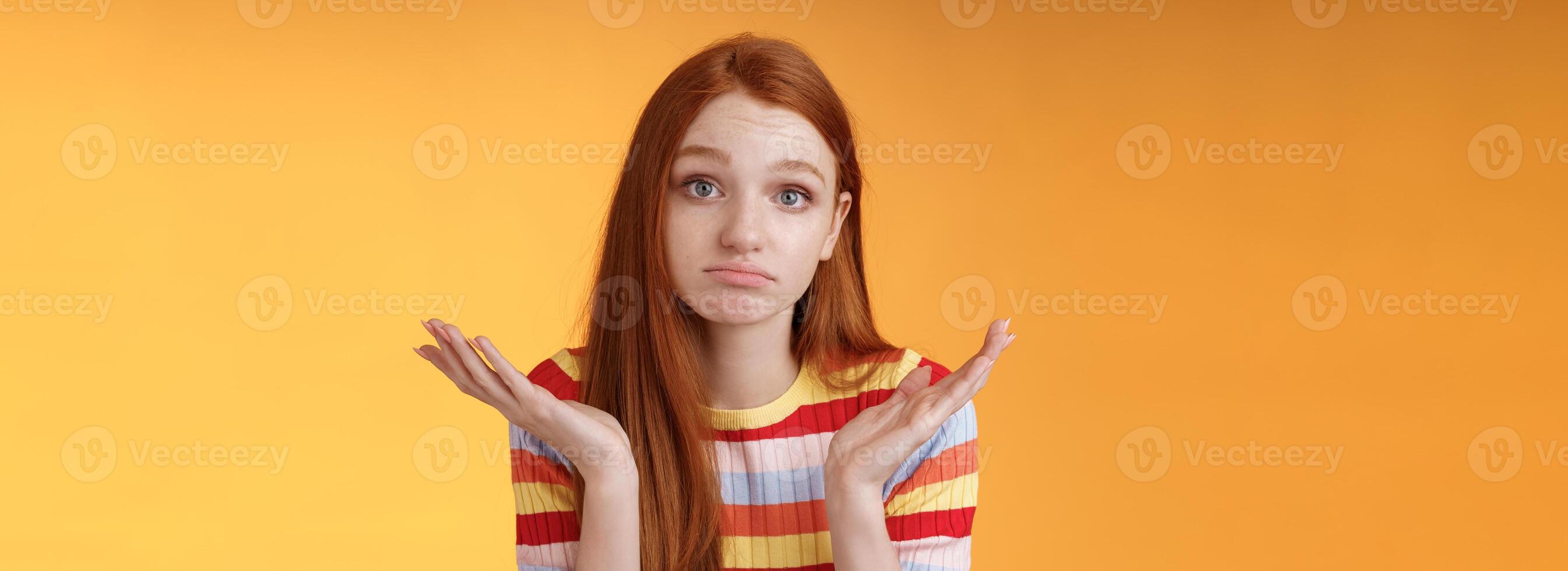 Clueless upset redhead young cute female coworker shrugging hands spread sideays unaware pouting confused cannot answer question apologizing not knowing, standing orange background photo