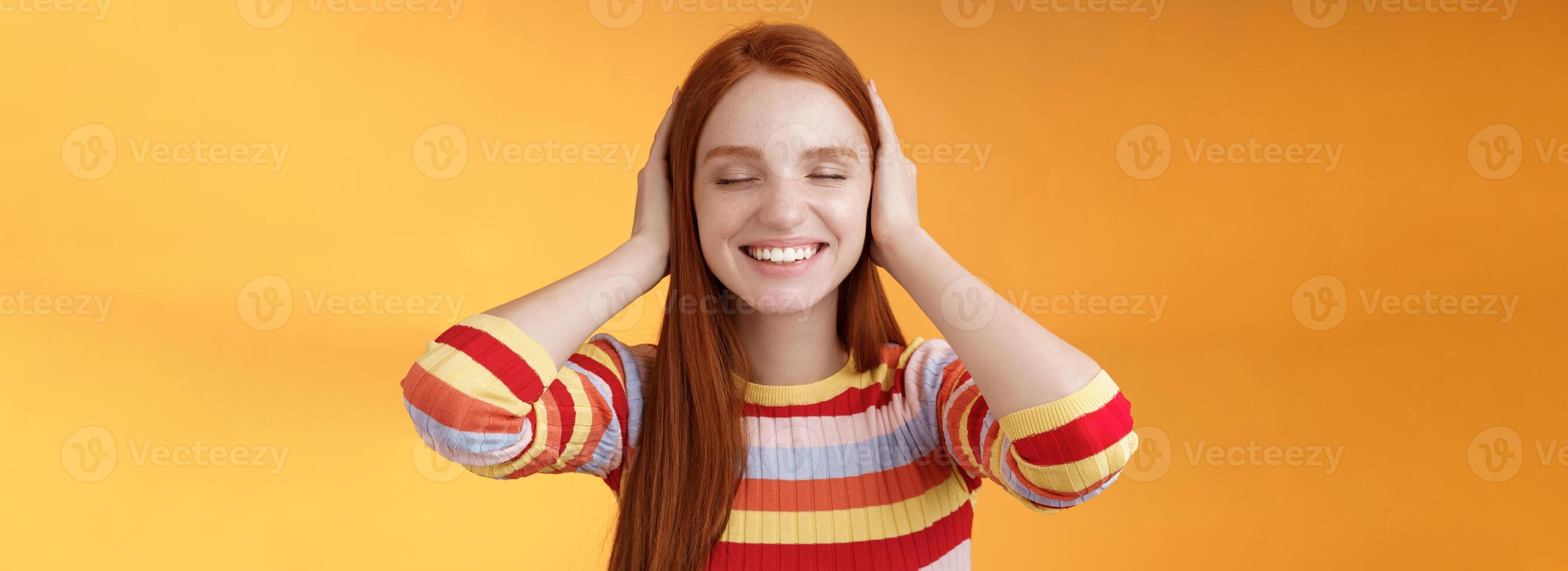 soñador carismático relajado oferta pelirrojo caucásico niña 20s cerca ojos cubrir orejas imagen lejos lejos, sonriente en general disfrutar silencio paz comodidad sin sonidos sin ruido, naranja antecedentes foto