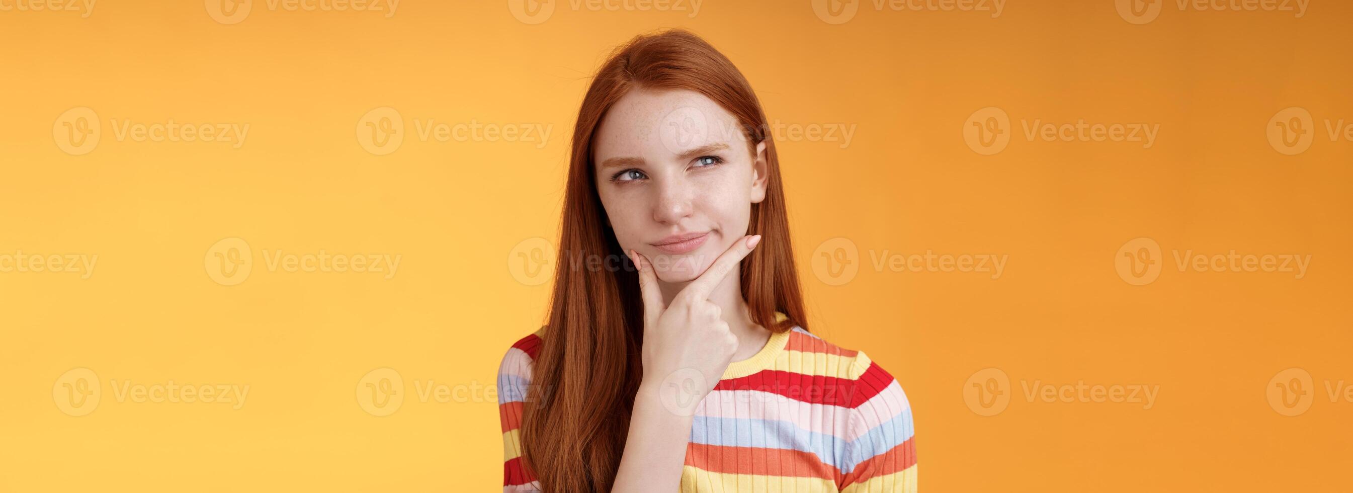 Hmm interesting. Suspicious doubtful attractive european redhead female pondering choice look hesitant thoughtful touch chin smirking tricky look upper left corner thinking, take decision photo