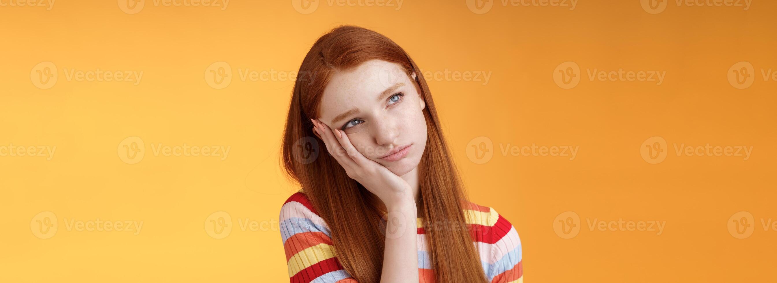 Lonely upset moody cute redhead girlfriend feeling boredom leaning palm look up pouting frowning displeased standing uneasy attend boring meeting, staring uninterested reluctant orange background photo