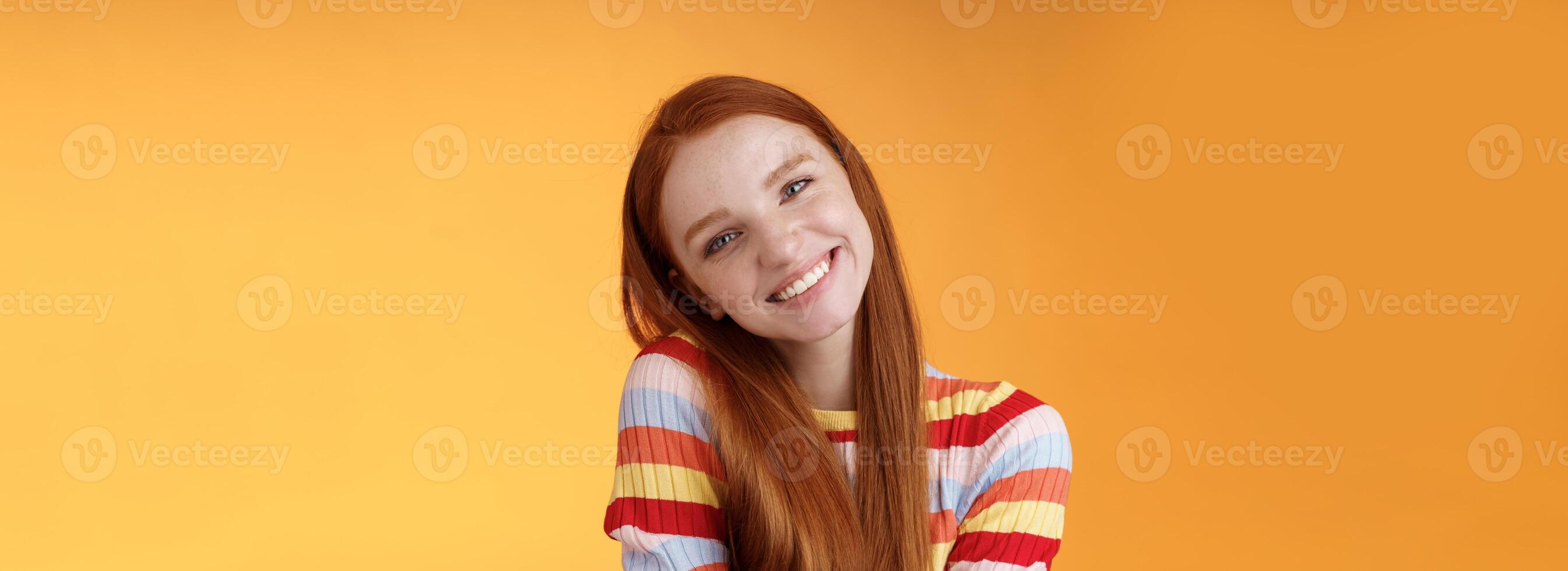 Tender lively cheerful smiling redhead european girl 20s tilting head leaning shoulder flirting grinning cute make lovely gazes camera coquettish talking boyfriend standing silly orange background photo