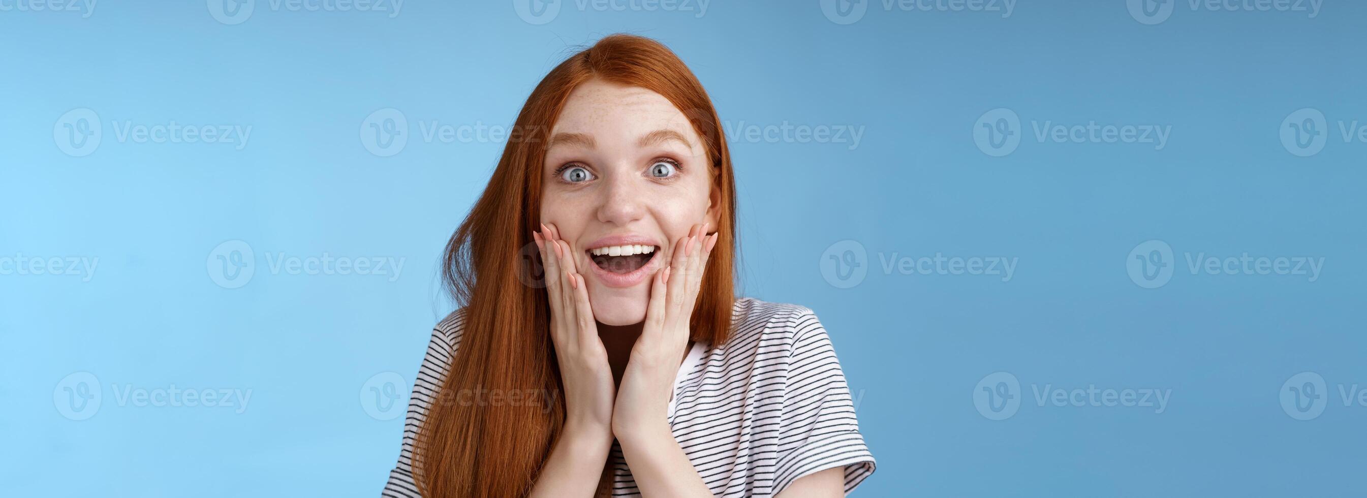 divertido contento soñador joven emocionado pelirrojo hembra ventilador mirando fascinado cámara sonriente admiración Encantado toque cara emocionado Rápido emocional alegre sorpresa, azul antecedentes foto