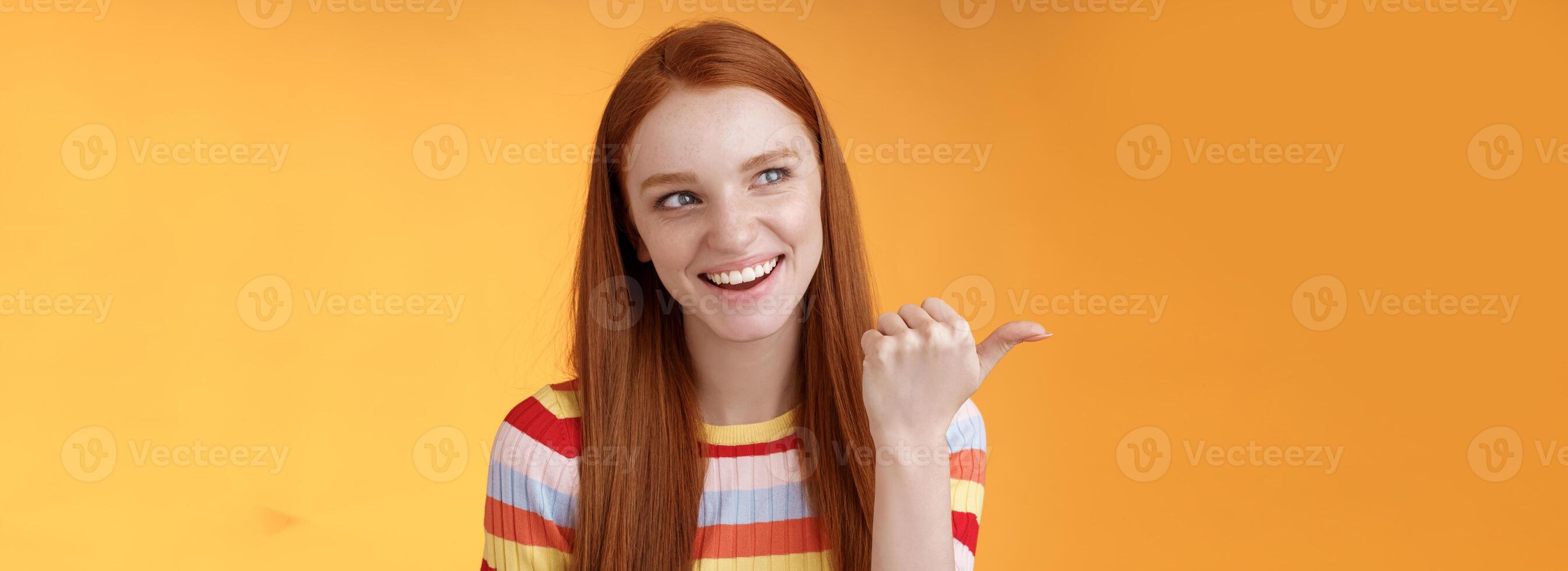 Amused outgoing redhead stylish female student discuss girly things smiling cheeky pointing handsome guy smirking devious pointing thumb looking intrigued curiously staring orange background photo