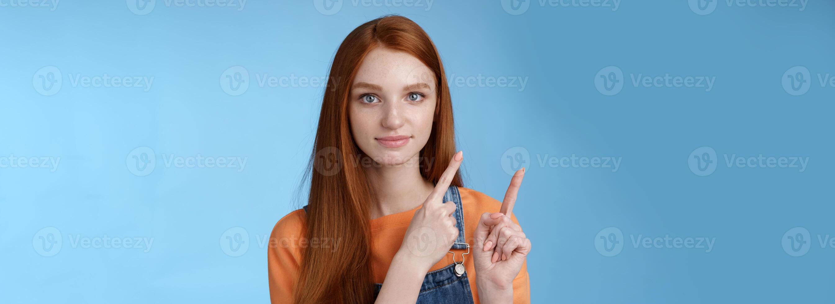 Assertive good-looking redhead girl know what talking about pointing upper left corner index fingers showing confidently good product recommend check out standing blue background photo