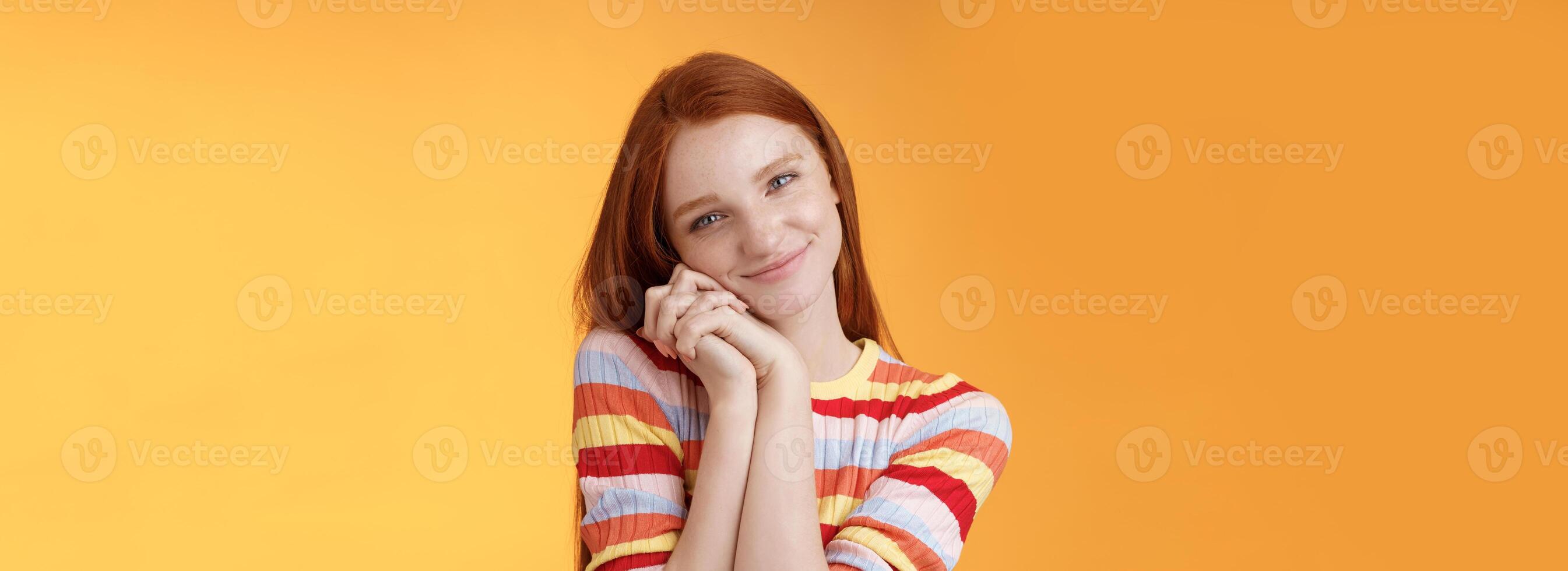 Sweet silly tender redhead young girl leaning palms touched smiling receive charming lovely gift standing thankful look affection sympathy accept dearest romantic gesture, orange background photo