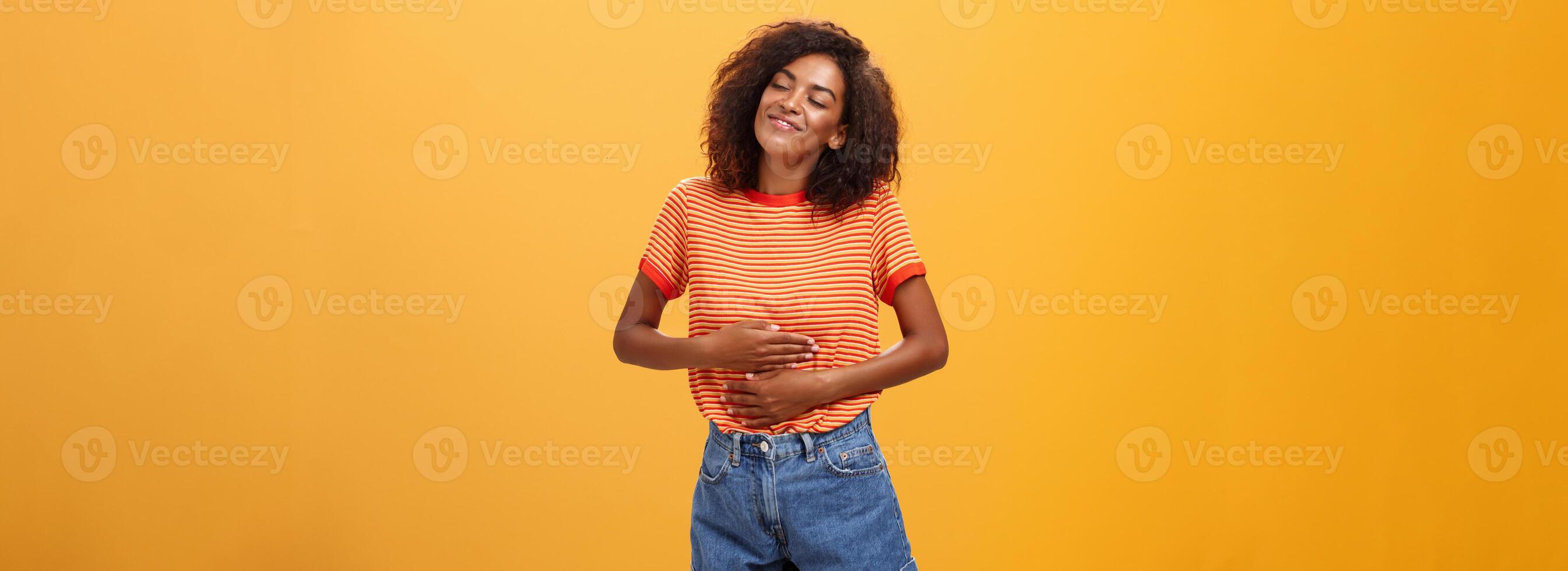 Mmm delicious meal warming me inside. Delighted stuffed good-looking stylish young female in striped t-shirt rubbing belly with satisfaction closing eyes from pleasure after eating tasty food photo