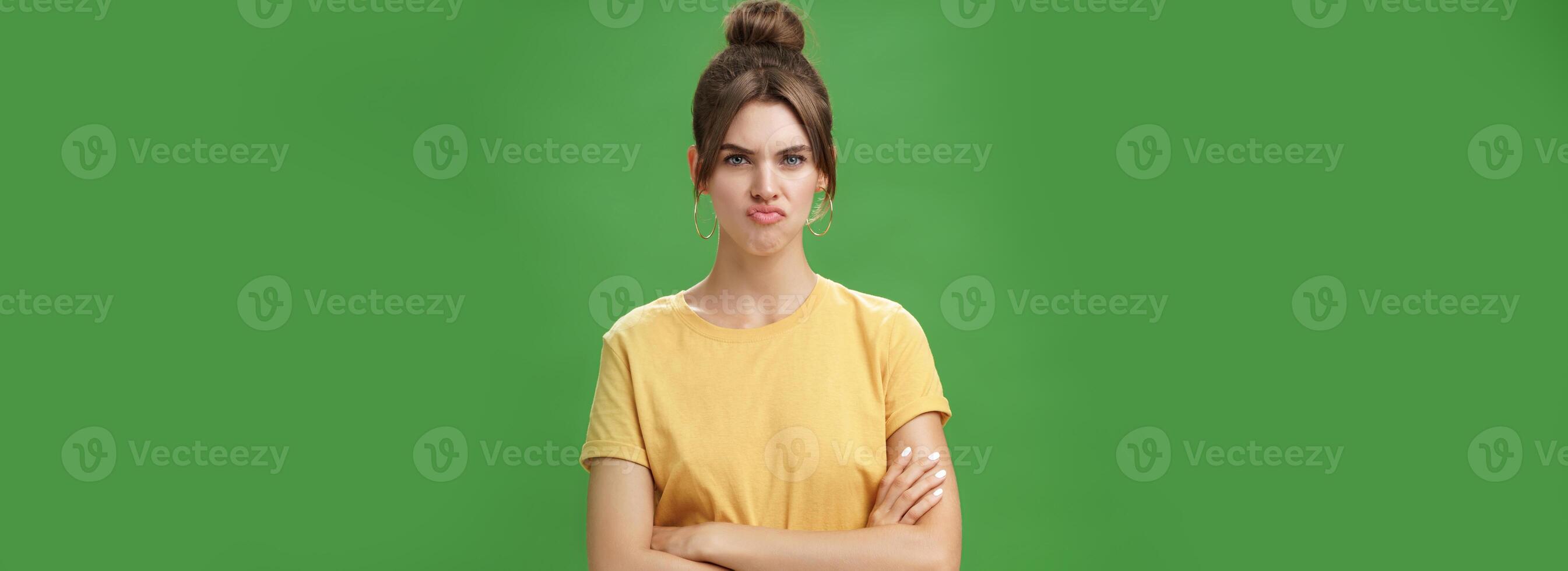 Girl not liking result of work looking displeased and serious at camera, frowning crossing hands against chest, pursing lips from disappointment, being offended over green background photo